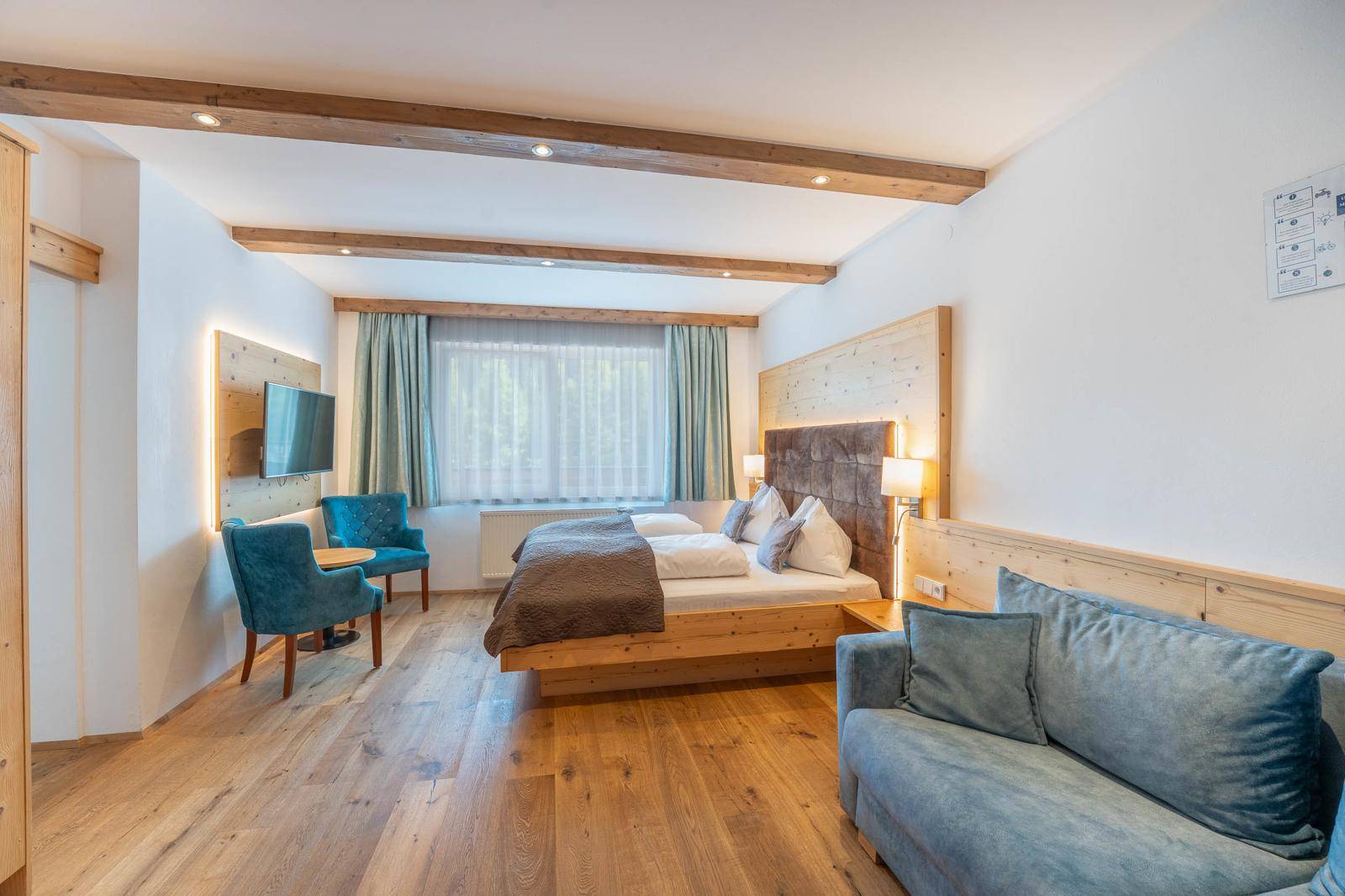 Helles Schlafzimmer mit Holzboden, Doppelbett und einem Sofa in Blautönen.