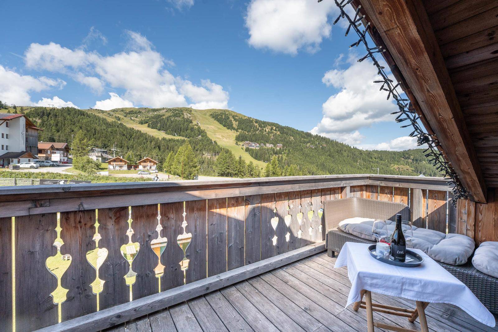 Großer Holzbalkon mit Sitzgelegenheiten und Panoramablick auf die Berge und Skipisten.