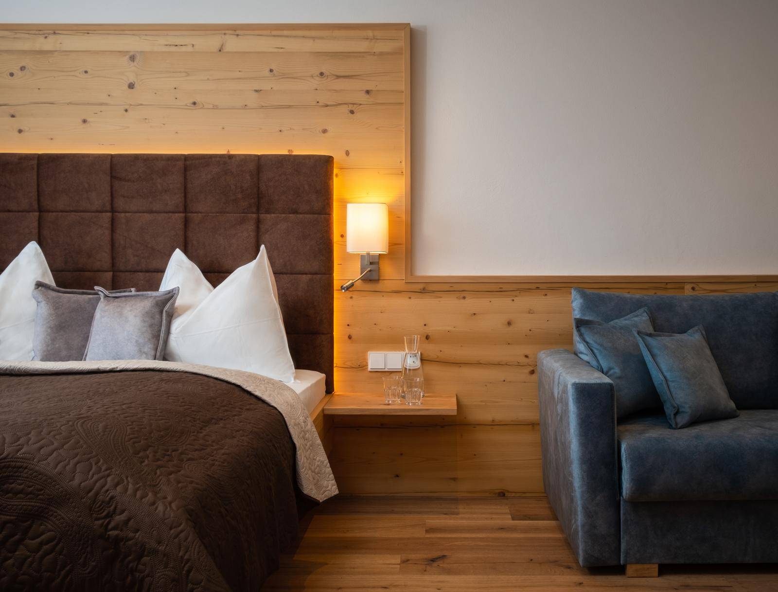 Detailansicht eines Bettes mit gepolstertem Kopfteil und einem blauen Sofa im Schlafzimmer.