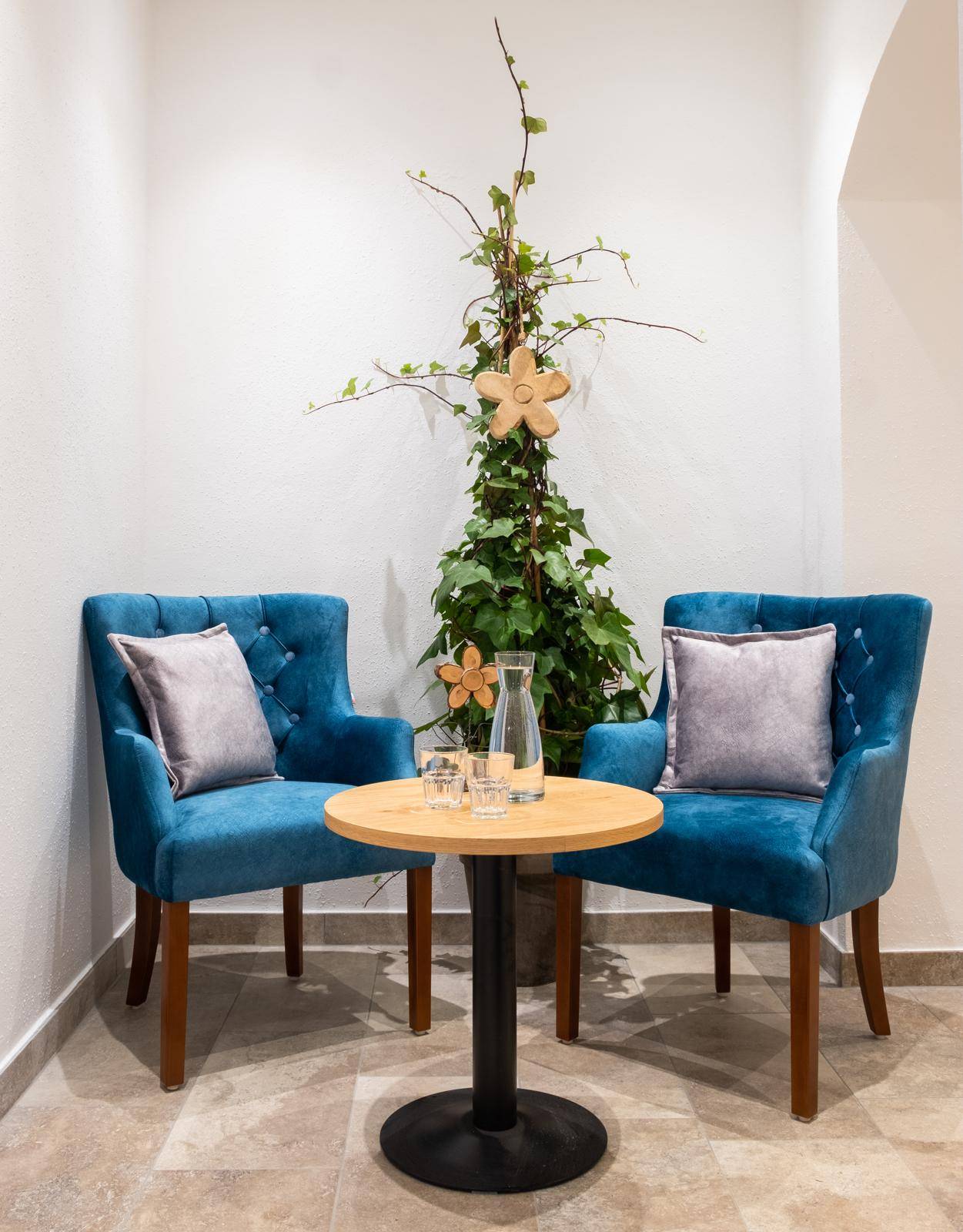 Kleiner Sitzbereich mit zwei blauen Sesseln, einem Holztisch und einer Pflanze.
