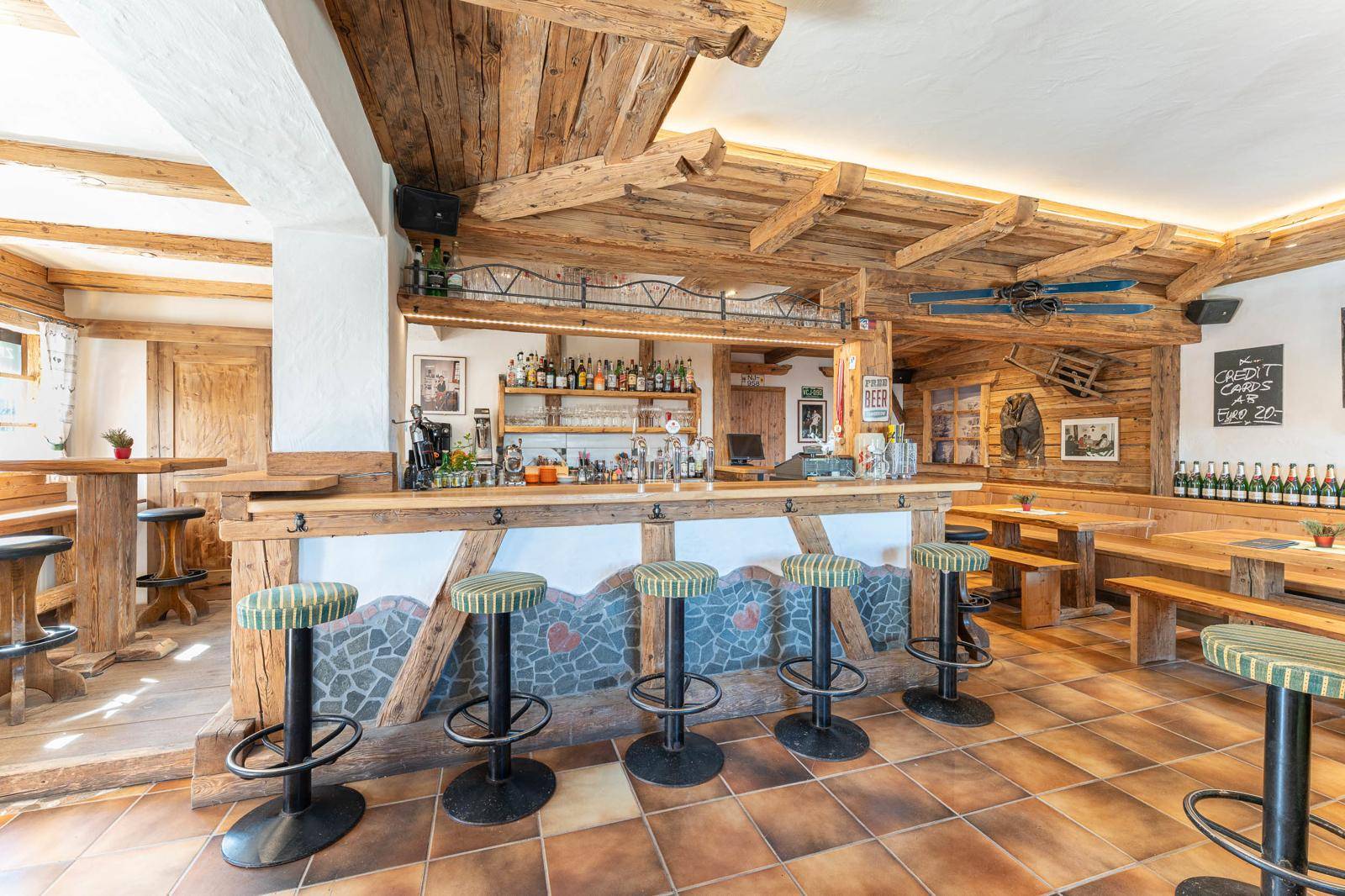 Rustikale Bar im alpinen Stil mit Holzbalken, Theke und gemütlichen Sitzgelegenheiten.