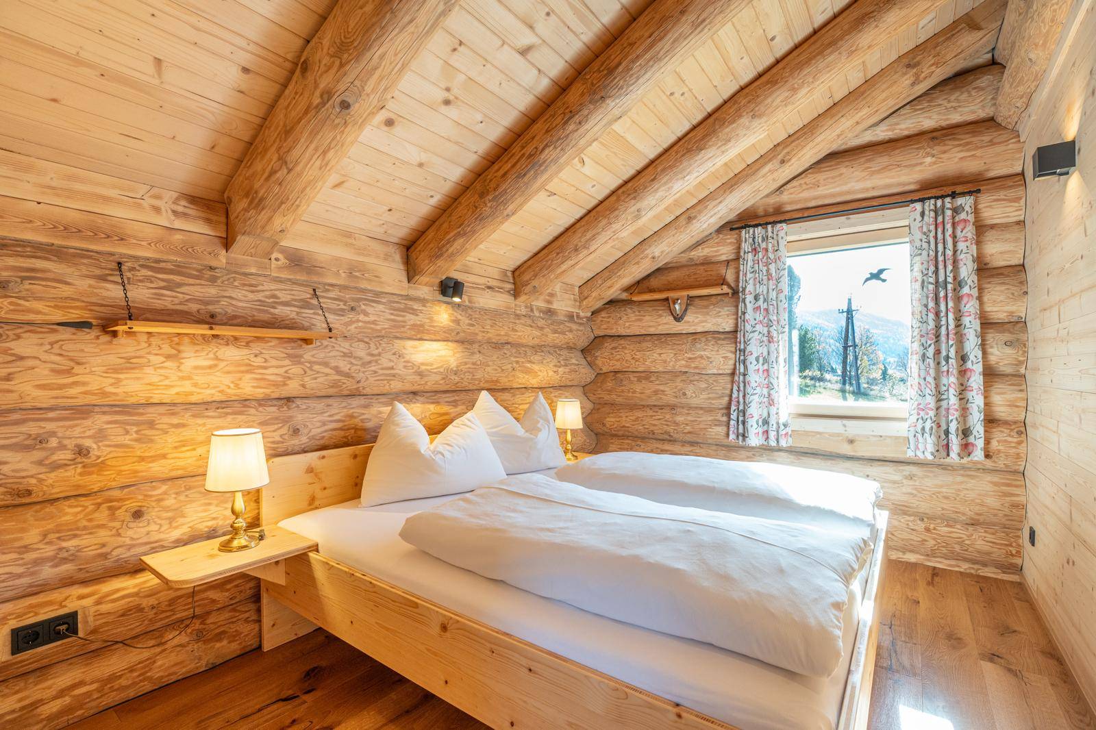 Helles Schlafzimmer mit Holzbalkendecke, Doppelbett und Fenster mit Bergblick.