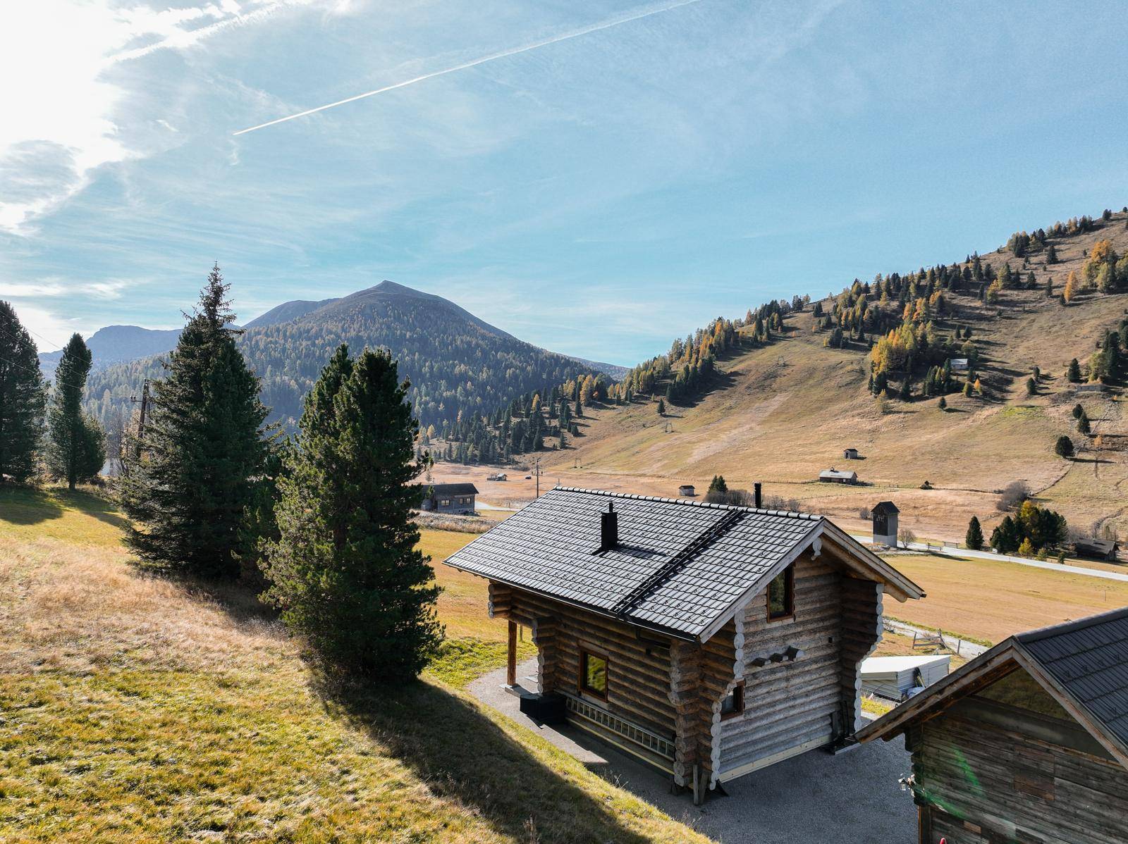 Rustikales Holzhaus in alpiner Berglandschaft unter blauem Himmel mit weiten Wiesen.