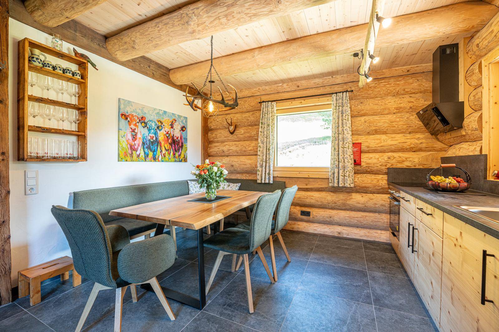 Offene Wohnküche mit Holztisch, Sitzbank und modernen Küchengeräten in rustikalem Ambiente.