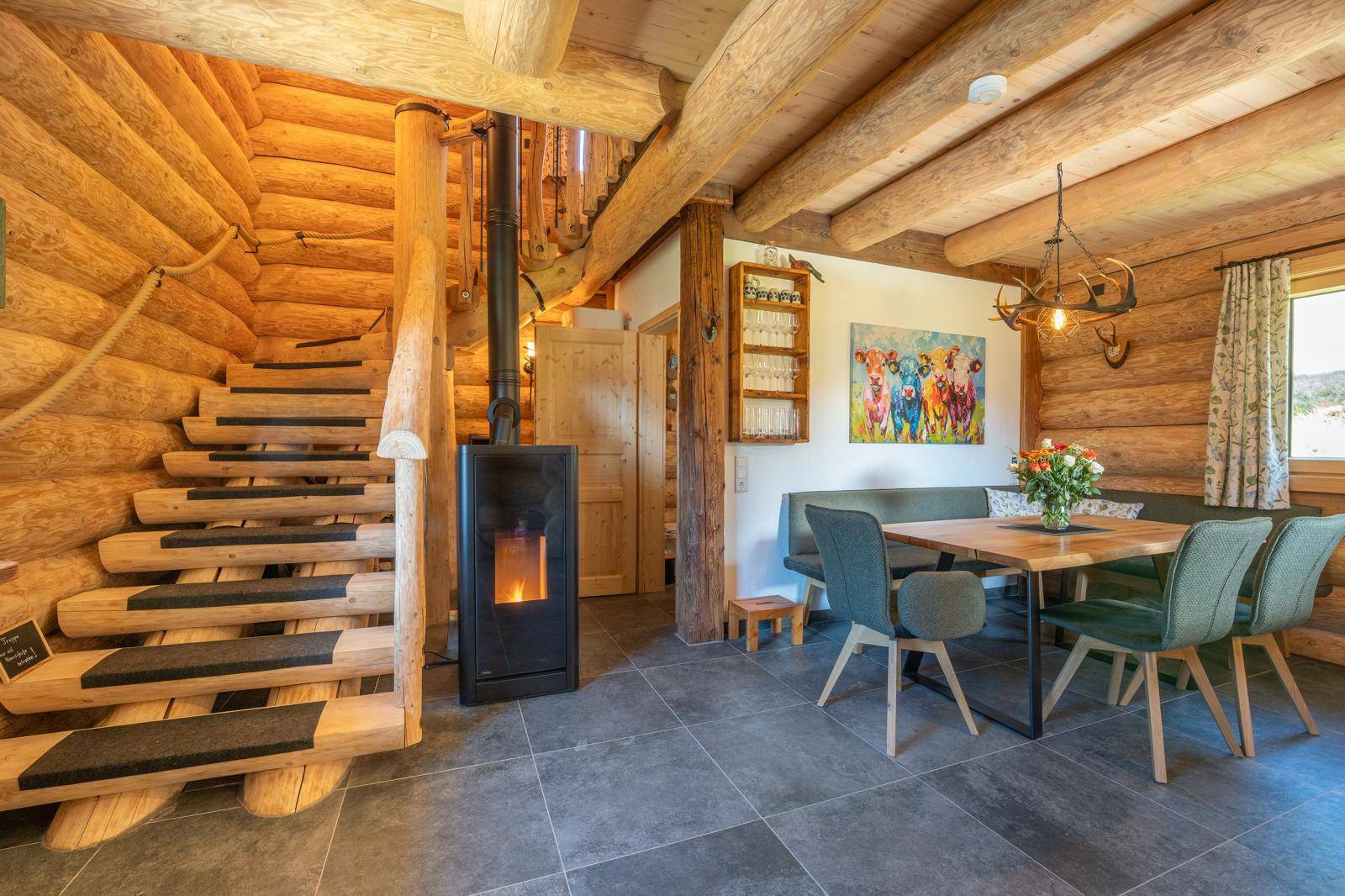 Gemütlicher Wohn-Essbereich mit Holzbalken, Kaminofen und rustikaler Holztreppe.