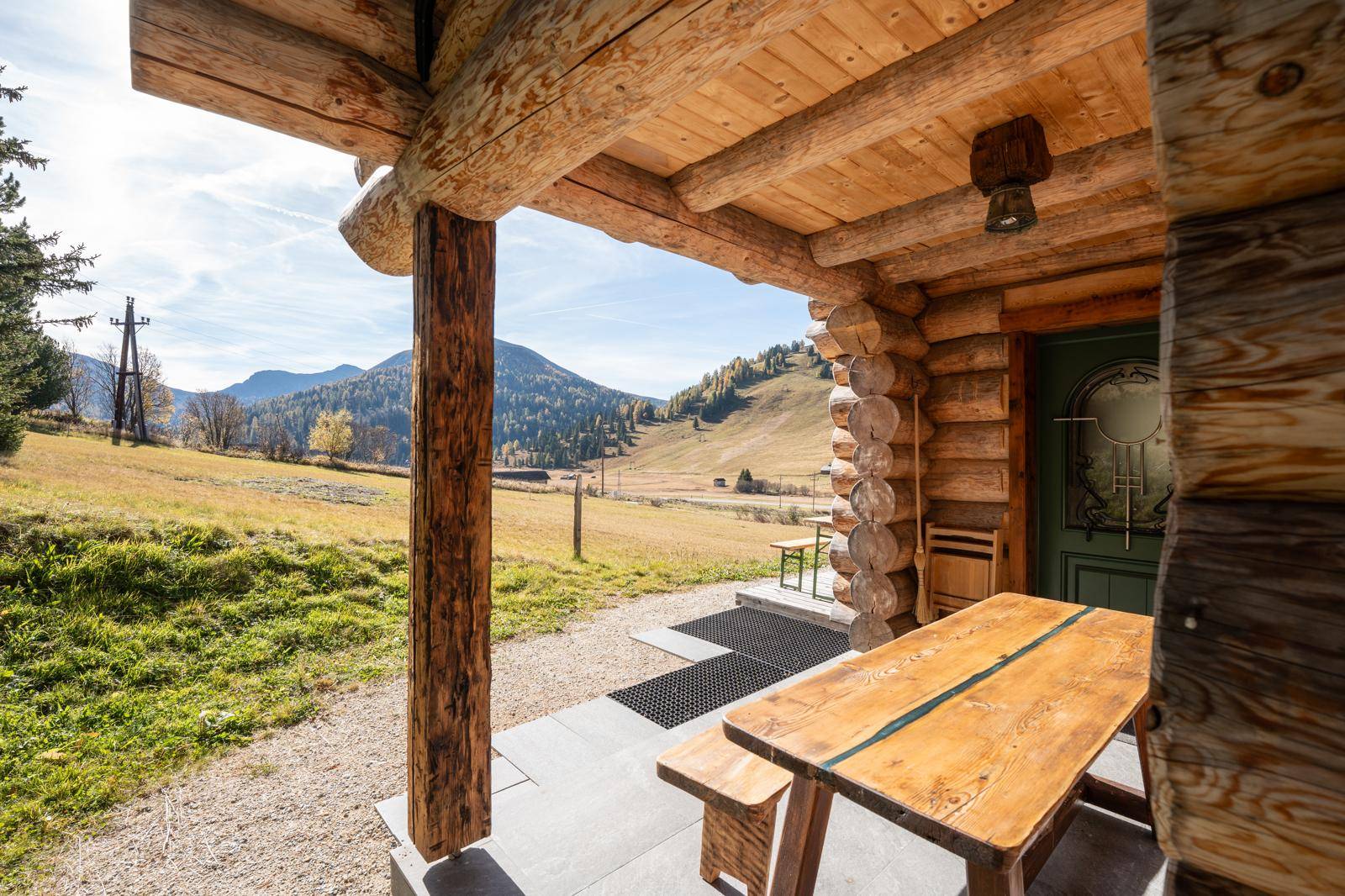 Überdachte Terrasse mit rustikalem Holztisch und Bänken, umgeben von Natur.