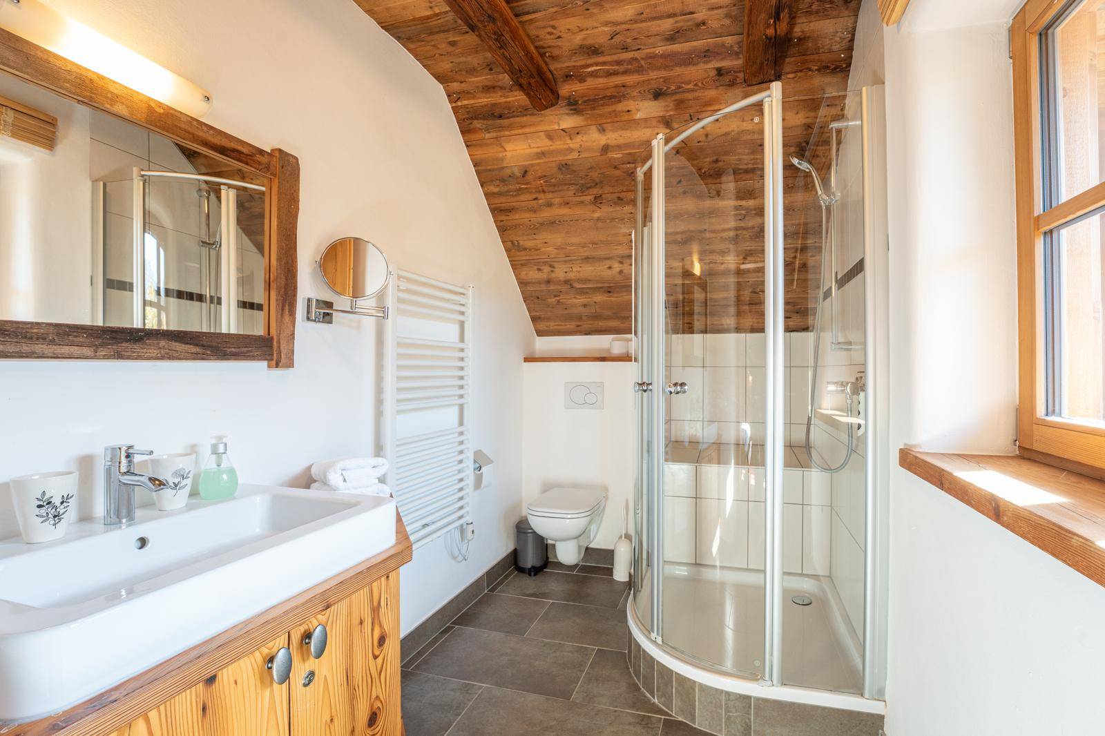 Modernes Badezimmer mit Duschkabine, WC, Holzwaschtisch und Fenster.