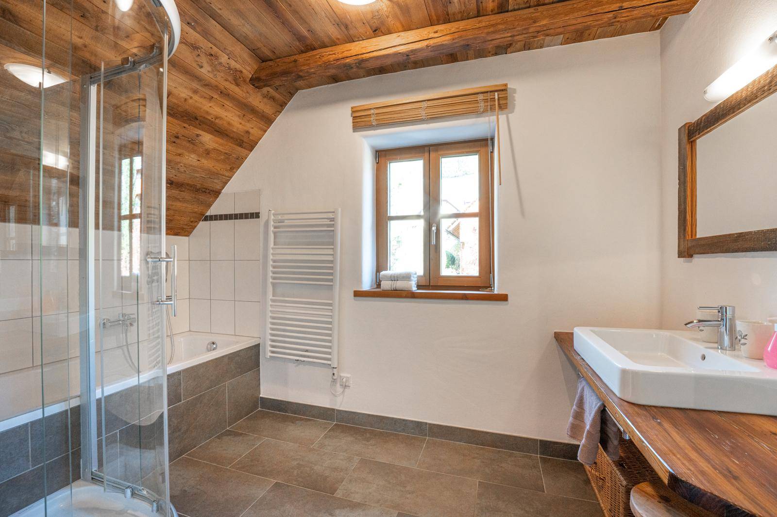 Helles Badezimmer mit Dusche, Badewanne, Holzwaschtisch und Dachschräge.