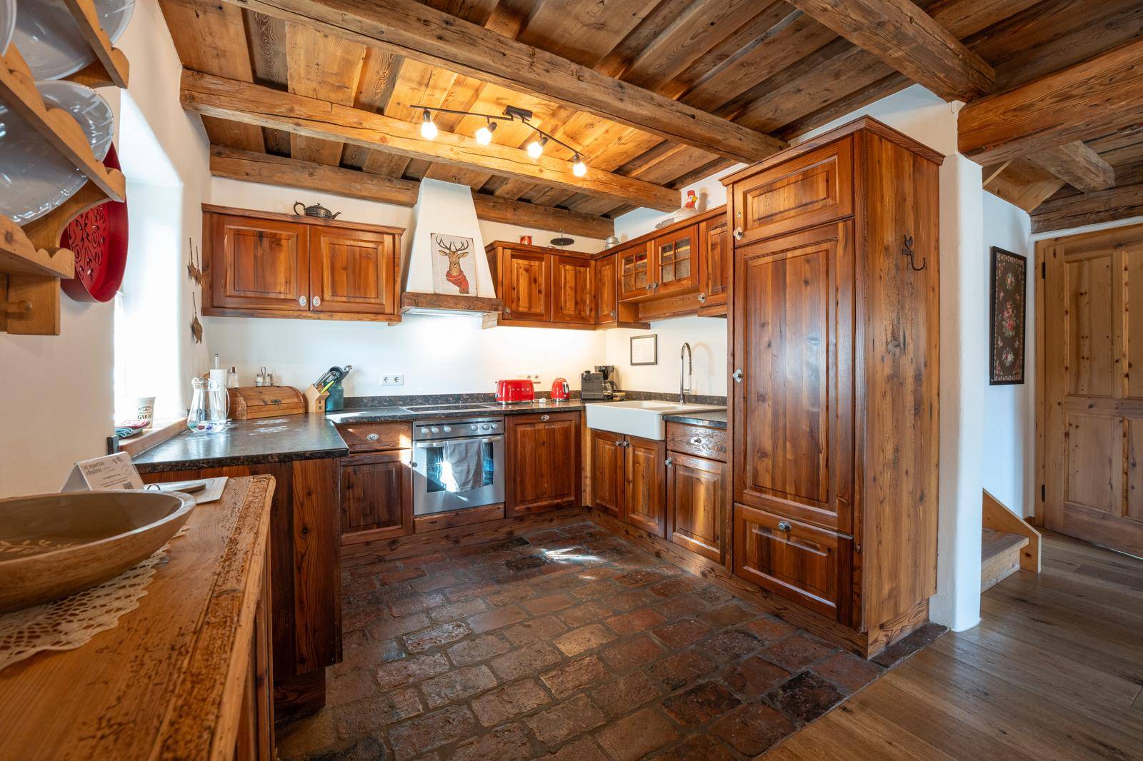 Rustikale Holzküche mit dunkler Arbeitsplatte, eingebauten Geräten und traditionellem Ziegelboden.
