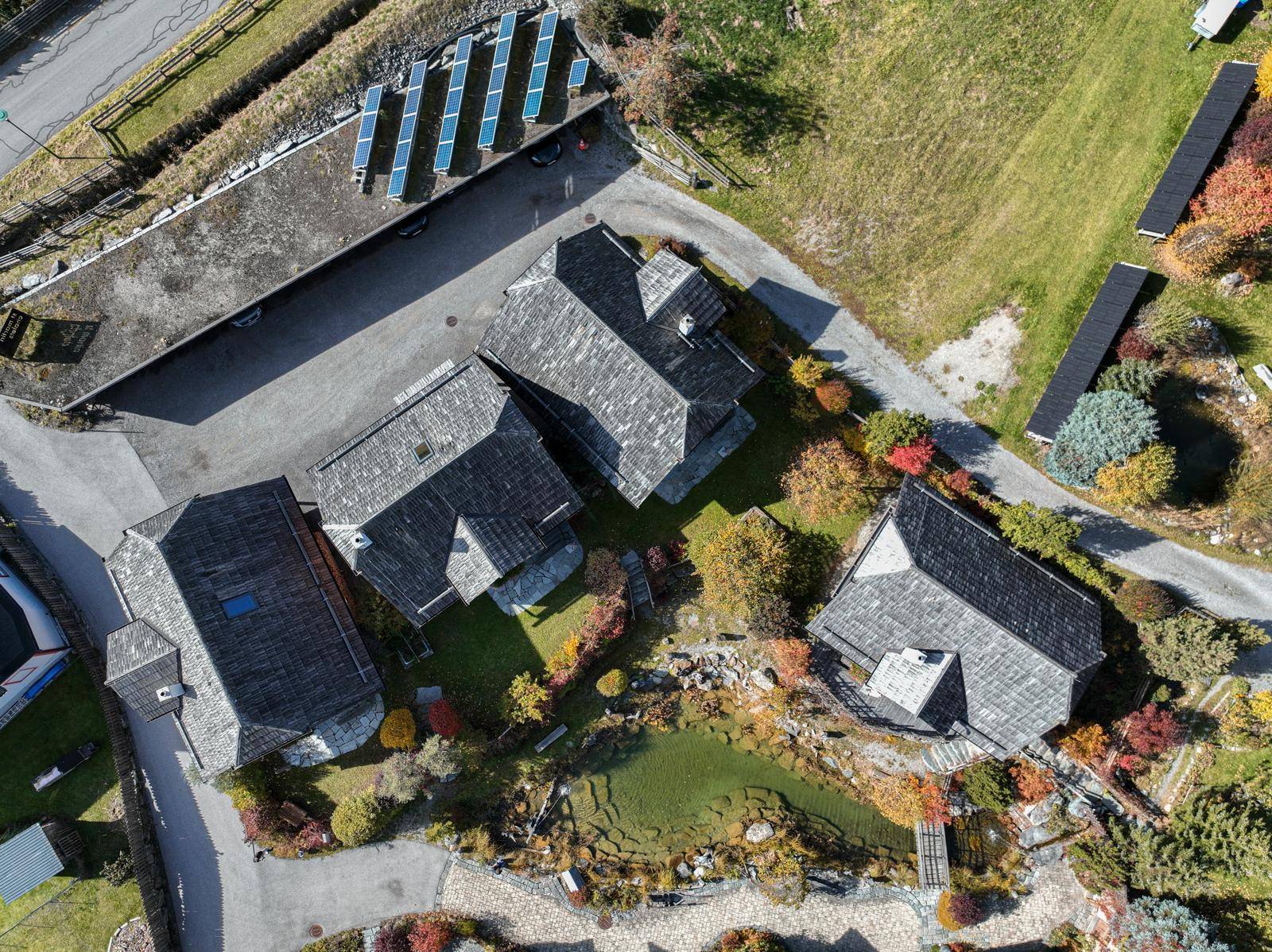 Luftaufnahme des Anwesens mit mehreren Gebäuden, Teich und Photovoltaikanlage auf dem Dach.
