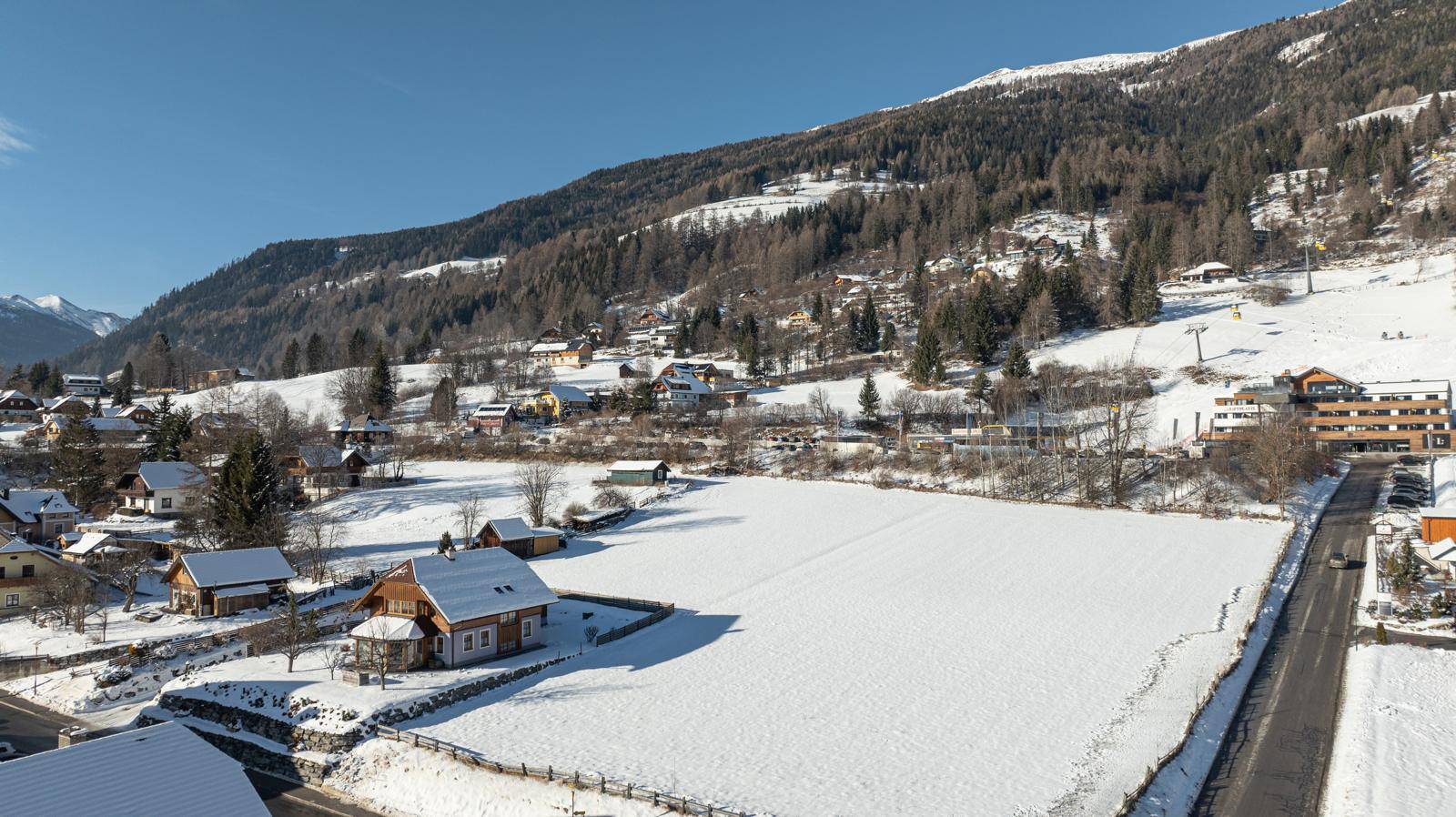 Panoramablick auf ein verschneites Dorf in den Bergen mit umliegenden Wäldern und Feldern.