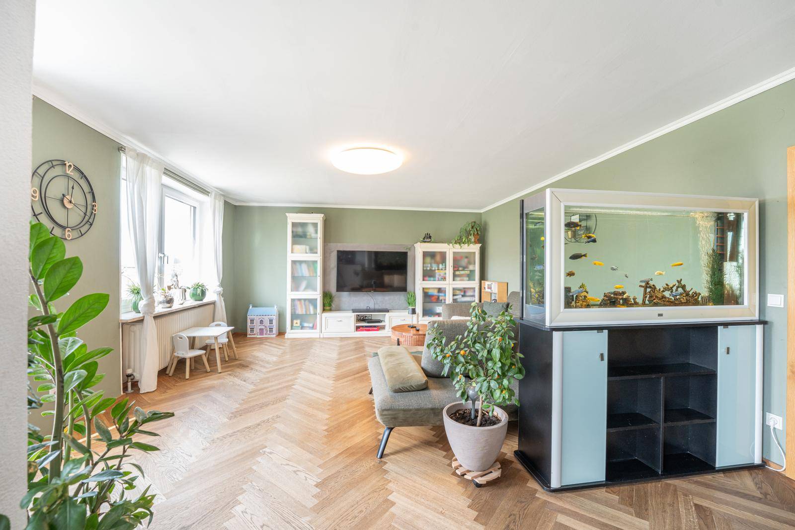 Helles Wohnzimmer mit Fischgrätparkett, großem Aquarium und viel Tageslicht durch die Fenster.