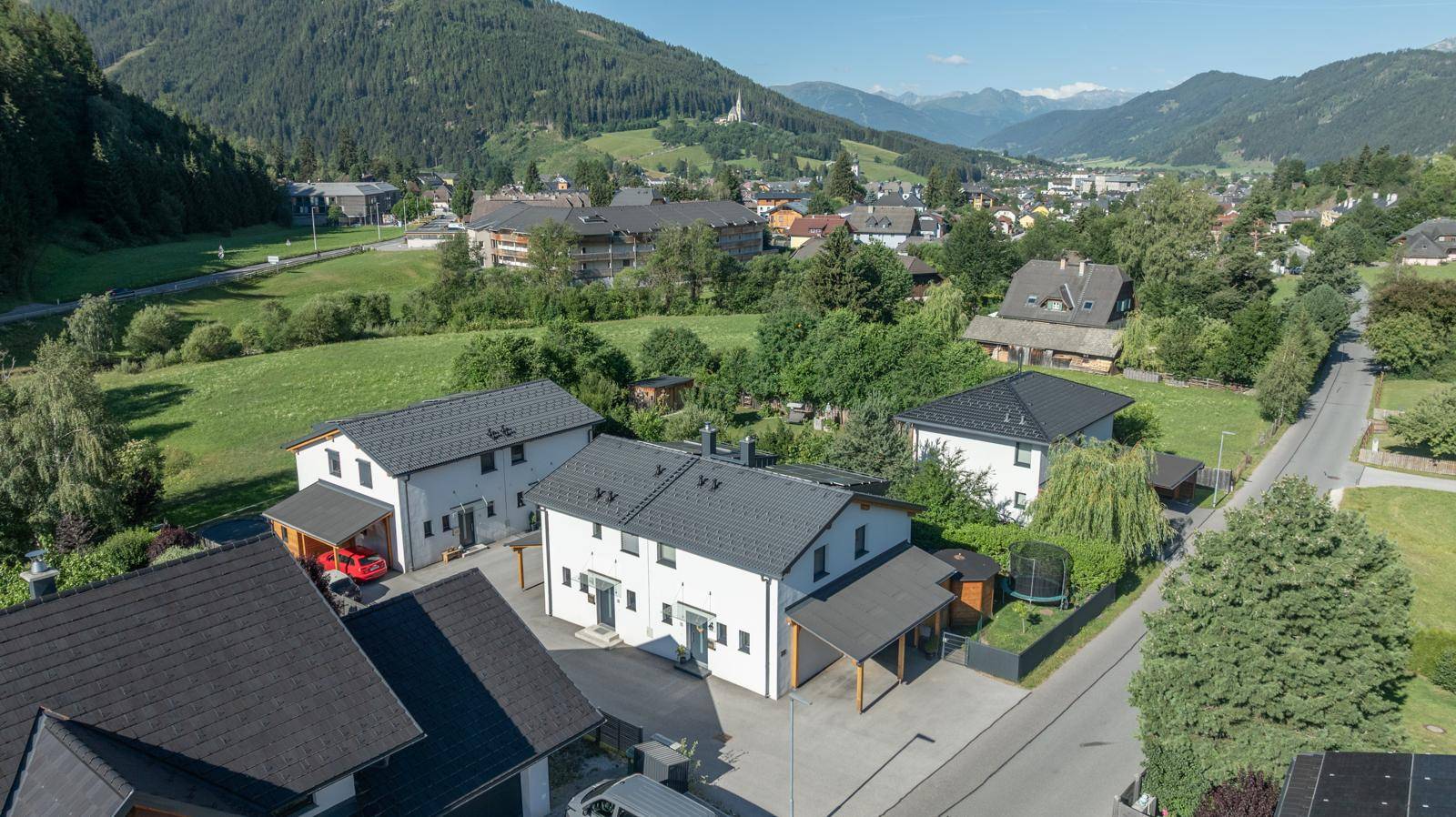 Luftaufnahme eines Wohngebiets mit Häusern, Straßen und Bergen im Hintergrund.