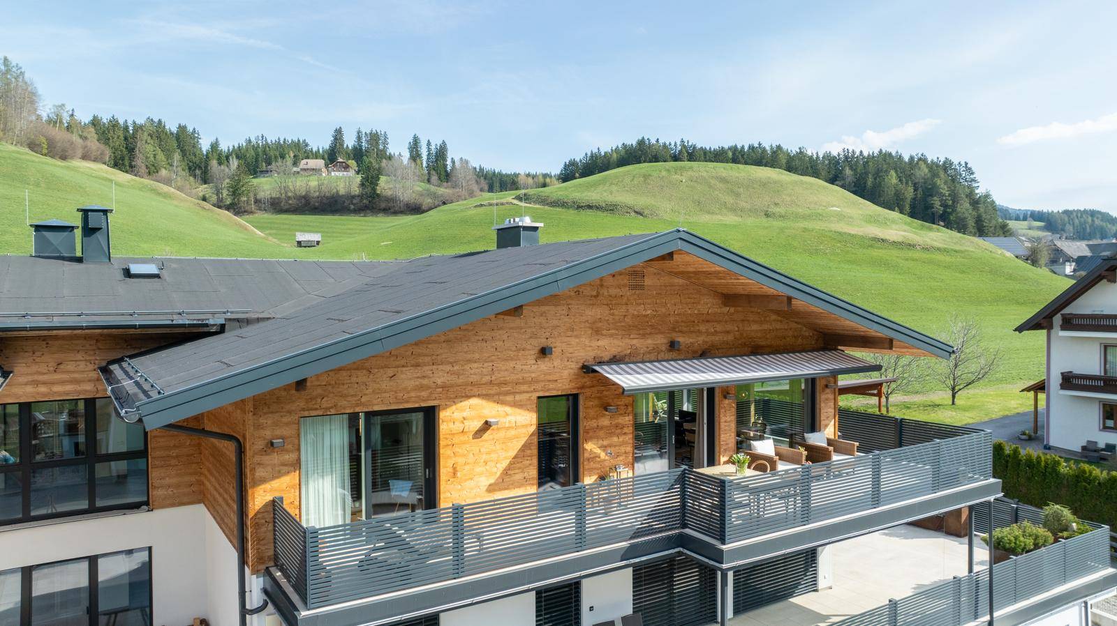 Modernes Gebäude mit Holzfassade, Balkonen und Blick auf die grüne Hügellandschaft.