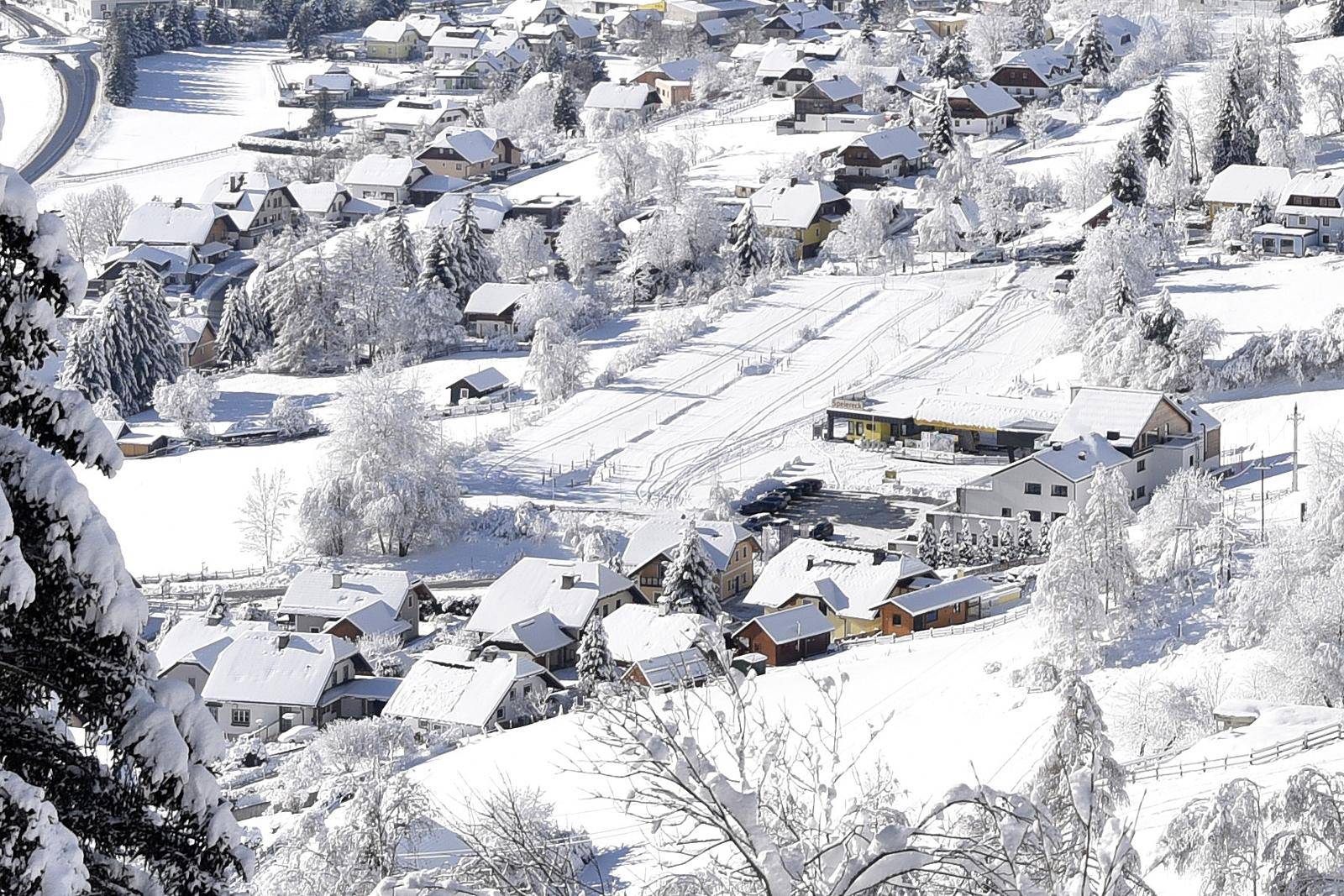 Eine winterliche Luftaufnahme einer Wohnsiedlung mit verschneiten Dächern und Bäumen.