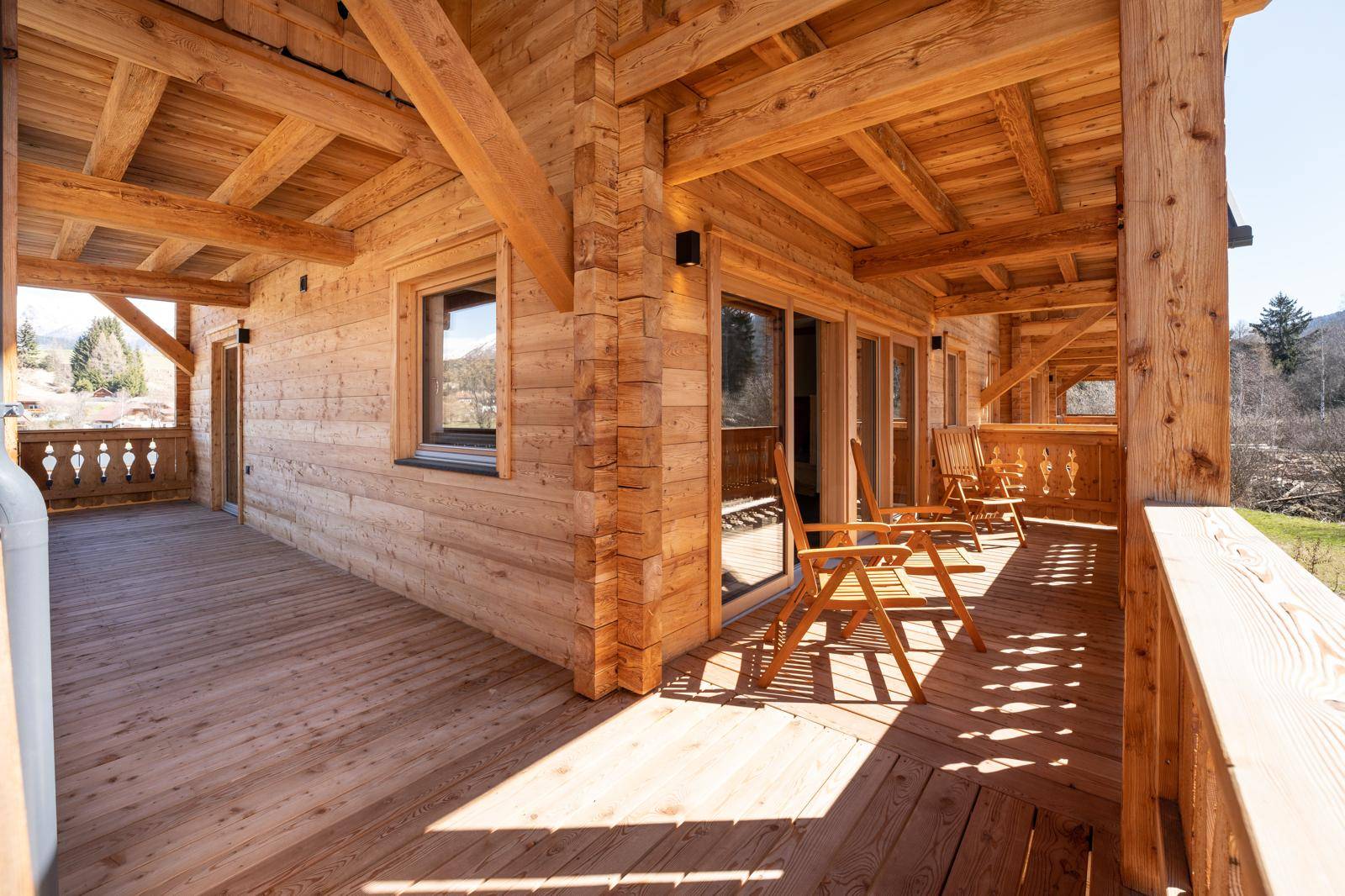 Geräumiger Holzbalkon mit Sitzgelegenheiten und sonnigem Ausblick auf die Umgebung.