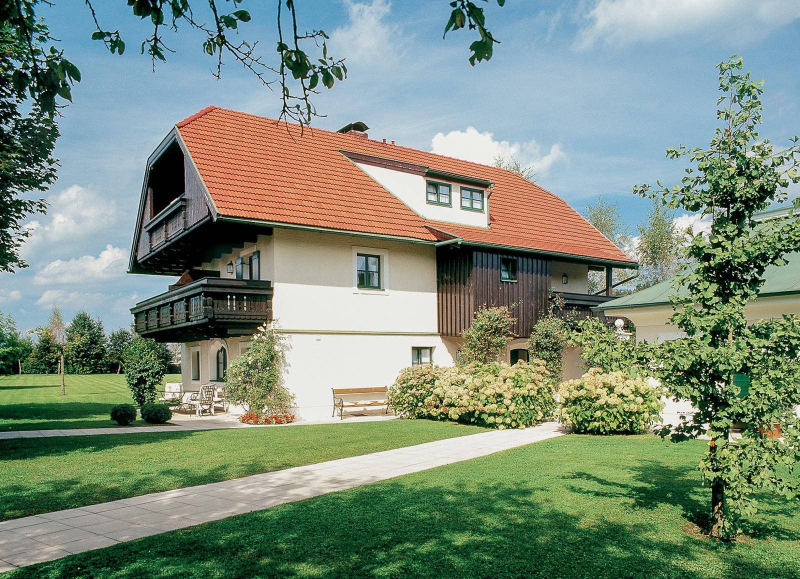 Gepflegter Garten mit Rasen, Gehwegen und traditionellem Gebäude mit Balkonen.