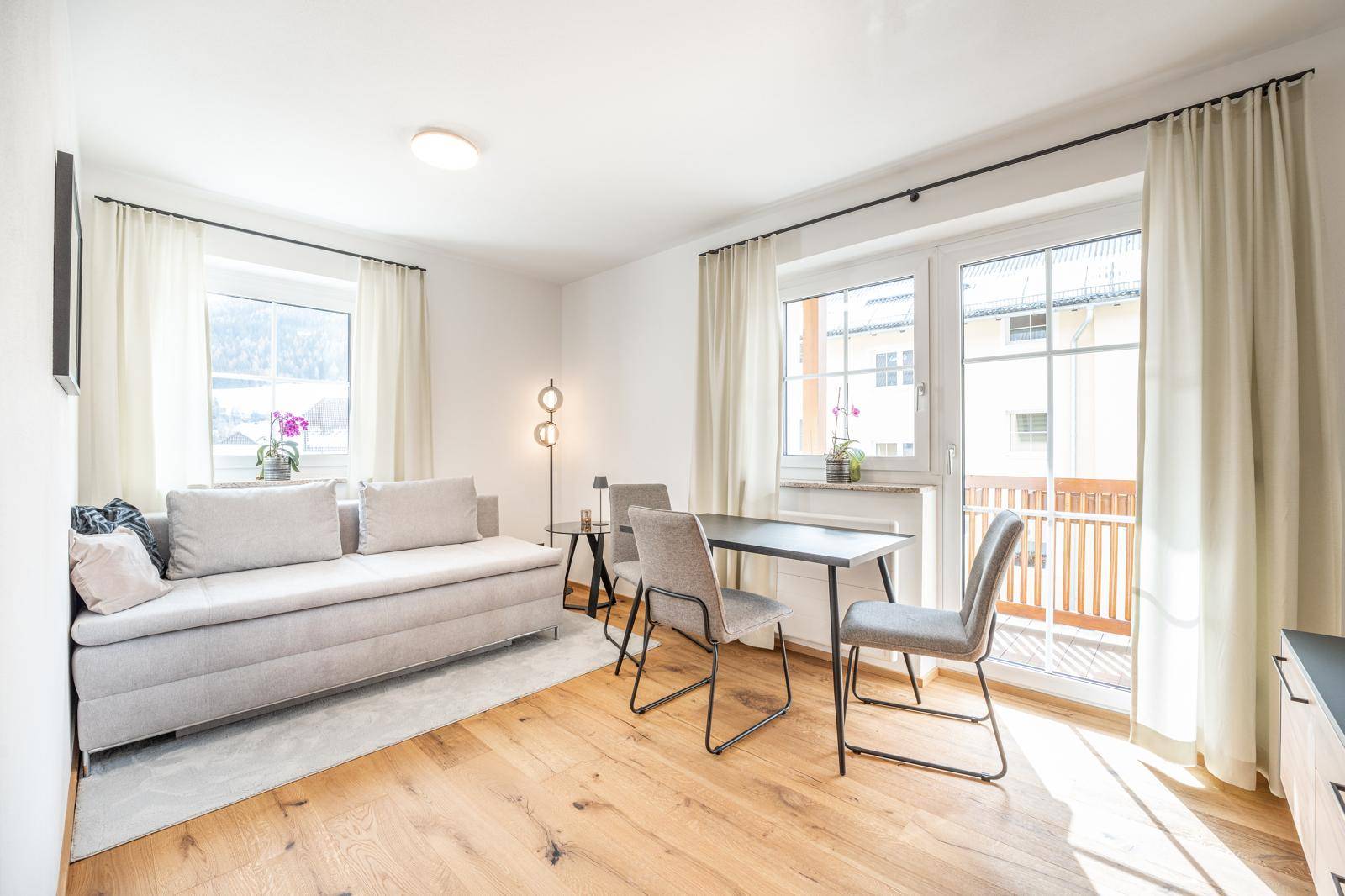 Helles Wohn- und Esszimmer mit Holzboden, bequemer Couch und Zugang zum Balkon.