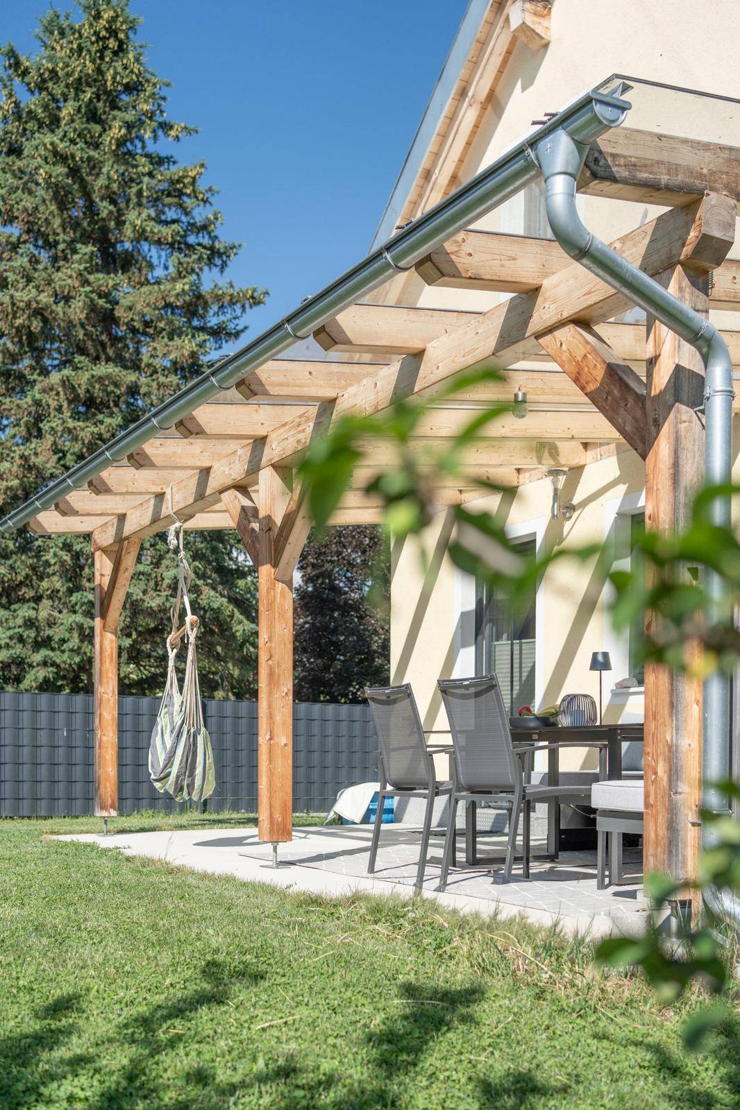 Überdachte Terrasse mit Holzpergola und Hängematte, umgeben von grünem Rasen.