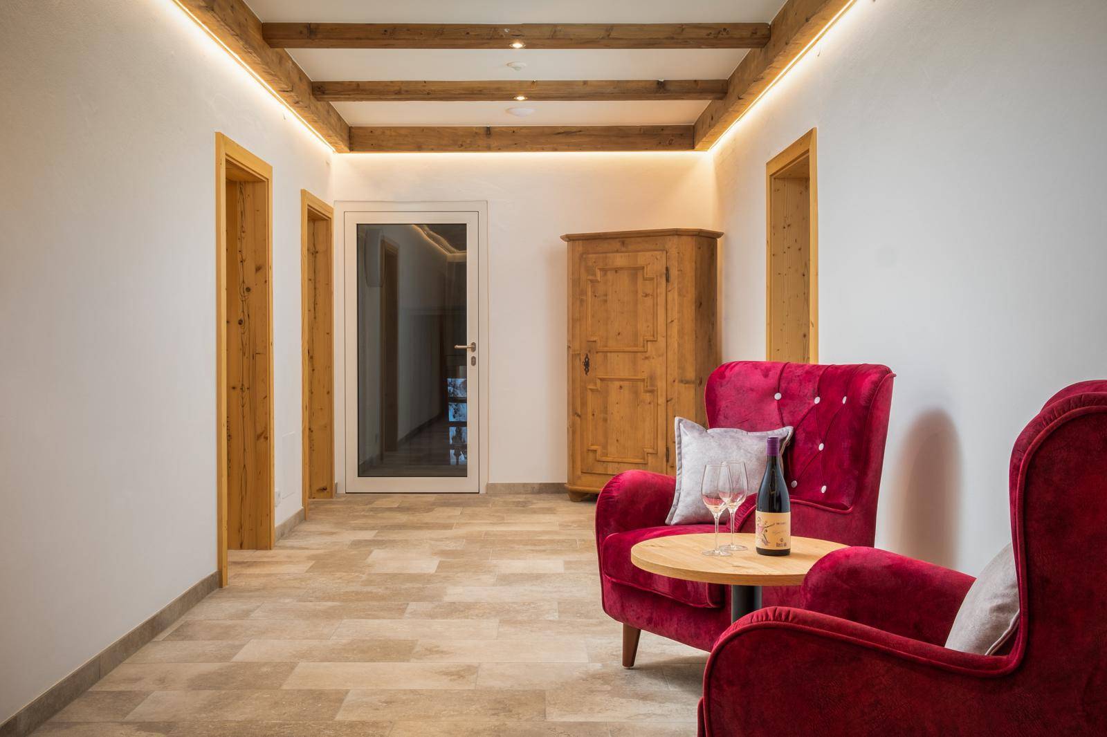 Heller Flur mit Holzbalkendecke, Fliesenboden und roten Samtsesseln.