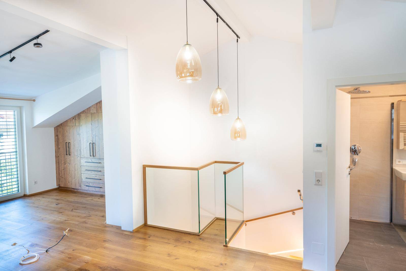 Heller Flur im Obergeschoss mit Holzboden, Glasgeländer und Blick ins Schlafzimmer.