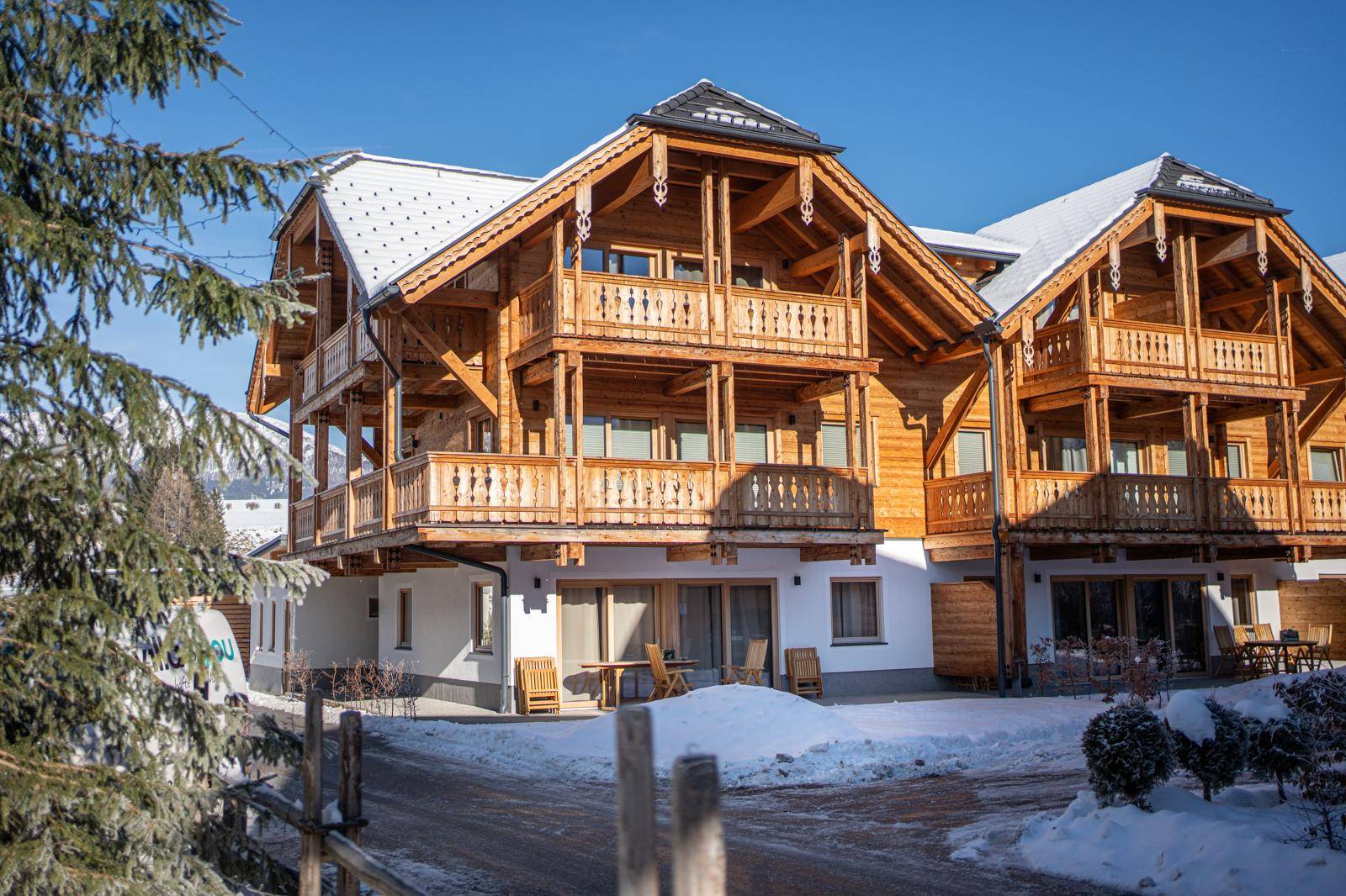 Sonnenbeschienenes Holzchalet mit traditionellen Balkonen und winterlicher Landschaft.