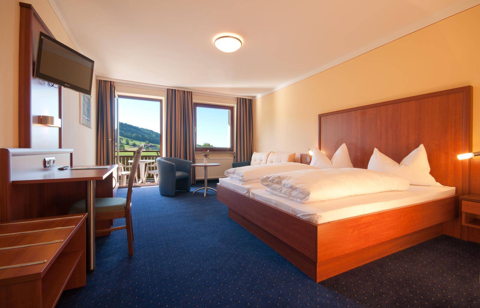 Helles Schlafzimmer mit Doppelbett, Schreibtisch und Zugang zu einem Balkon mit Landschaftsblick.