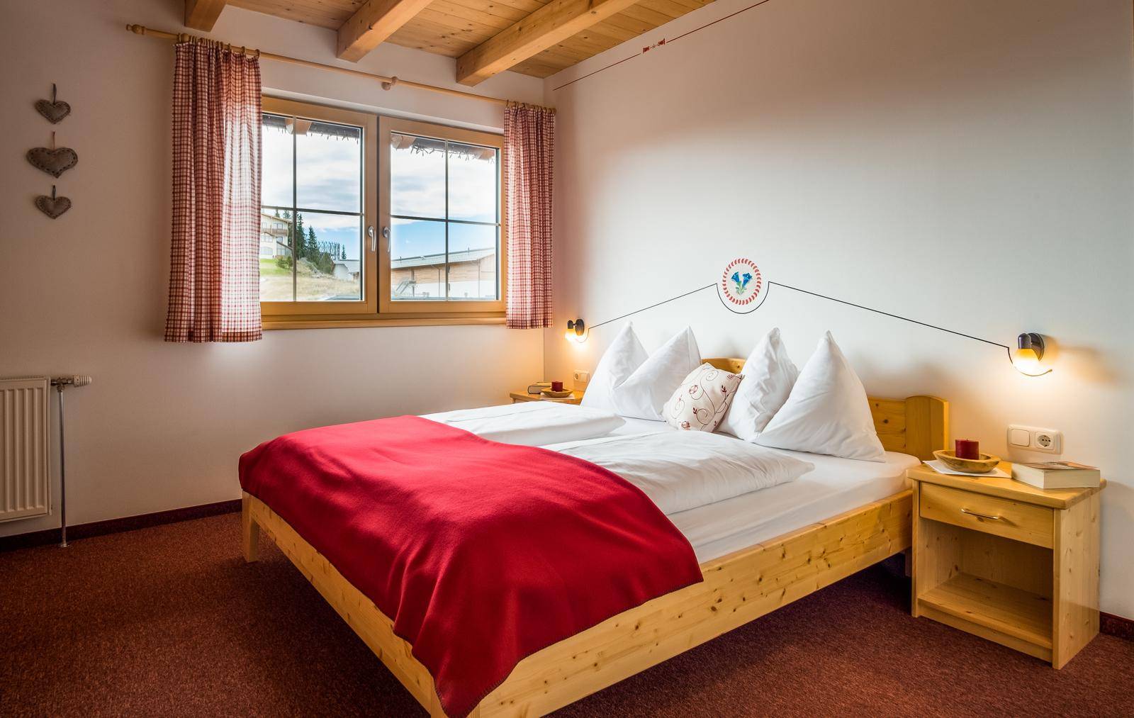 Helles Schlafzimmer mit Doppelbett, Holzmöbeln und Fensterblick auf die Berglandschaft.