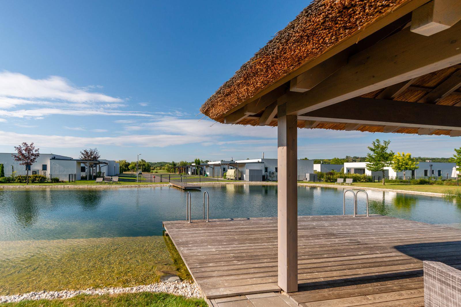 Holzterrasse mit Reetdach-Pavillon direkt am Wasser, ideal zum Entspannen.