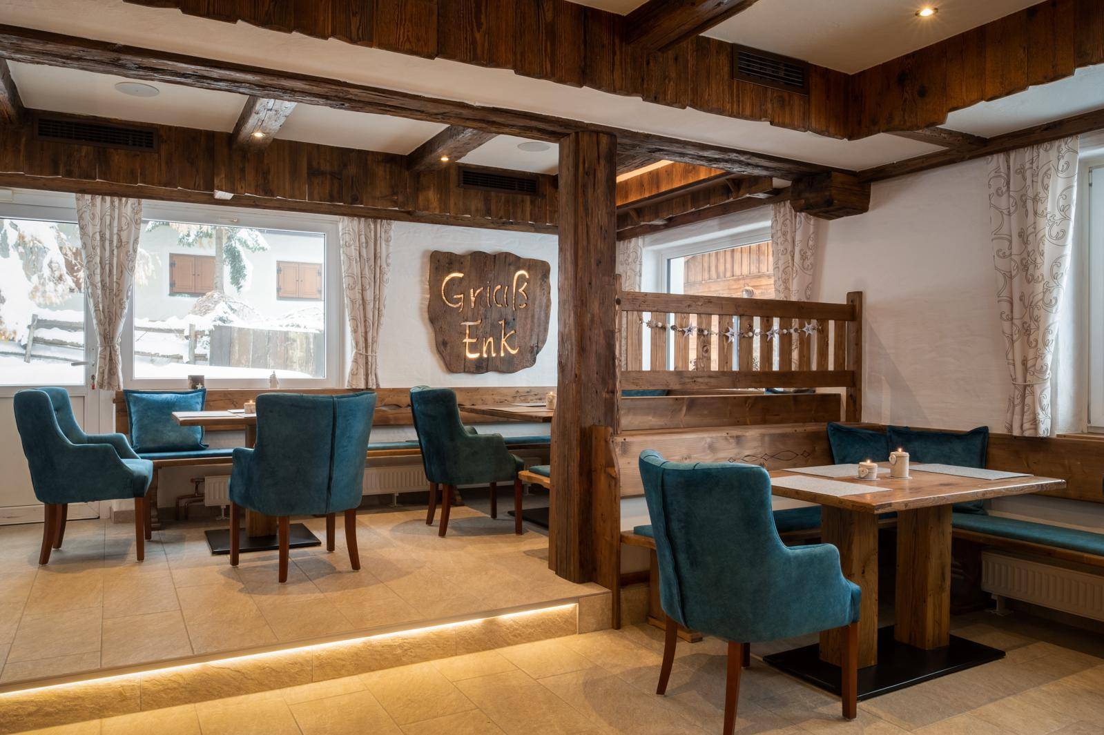 Rustikaler Essbereich mit Holzbalken, blauen Sitzgelegenheiten und großen Fenstern.