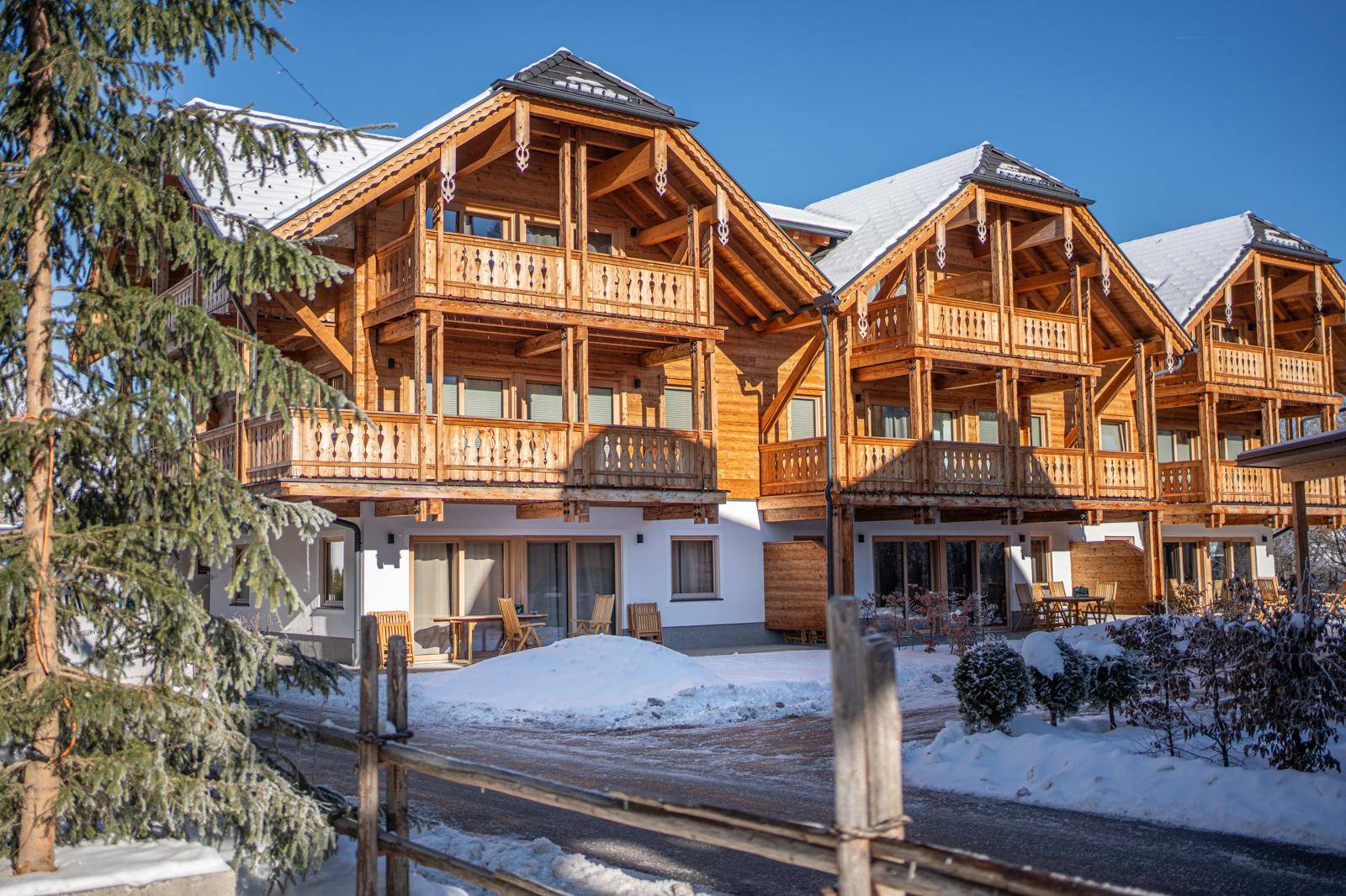 Charmantes Holzchalet mit mehreren Balkonen und schneebedecktem Dach unter blauem Himmel.