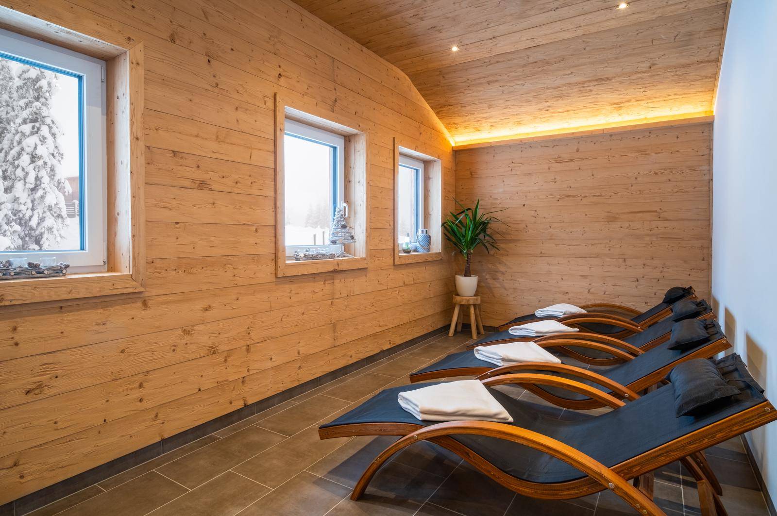 Entspannungsbereich mit Holzvertäfelung, Liegestühlen und Fenstern mit Blick auf die verschneite Landschaft.