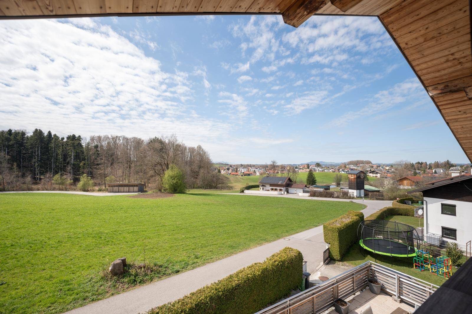 Weitläufiger Blick vom Balkon über grüne Felder und die umliegende Landschaft unter blauem Himmel.