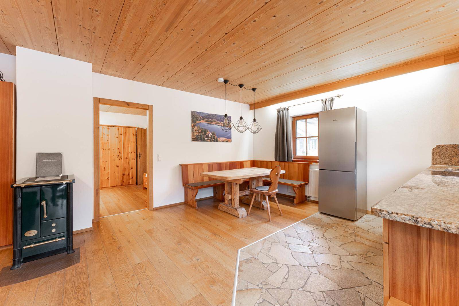Rustikaler Wohn-Essbereich mit Holzboden, traditionellem Ofen und integrierter Sitzecke.