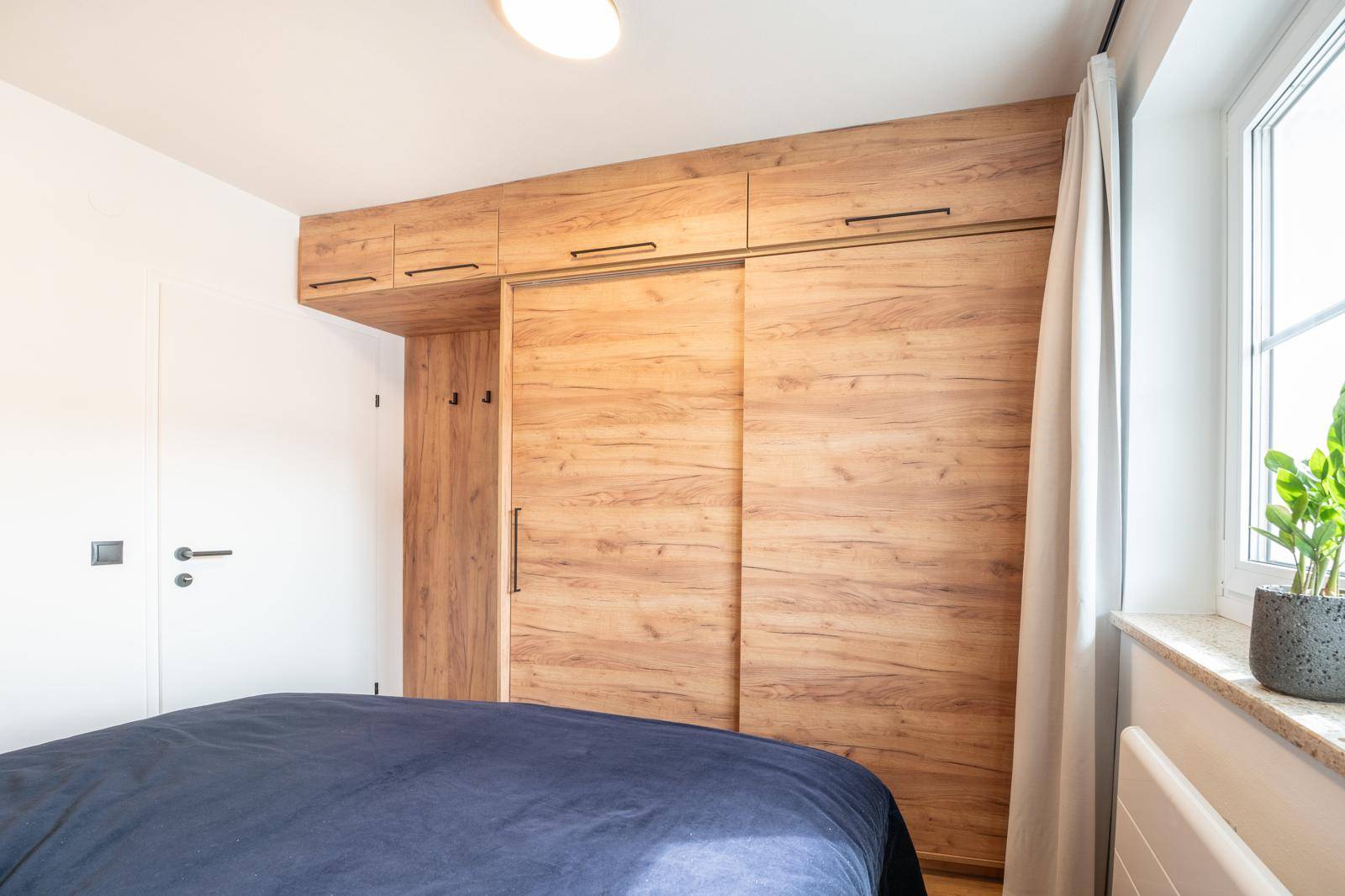Schlafzimmer mit großem Einbauschrank aus Holz und hellem Fenster.