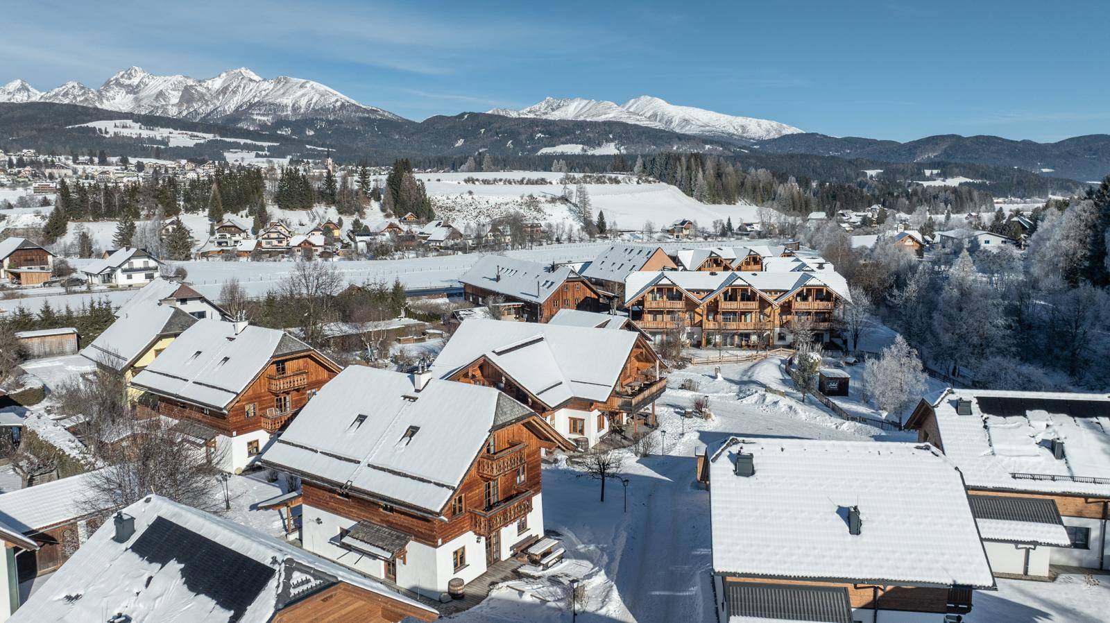Luftaufnahme einer winterlichen Wohnsiedlung mit verschneiten Dächern und majestätischem Bergblick.