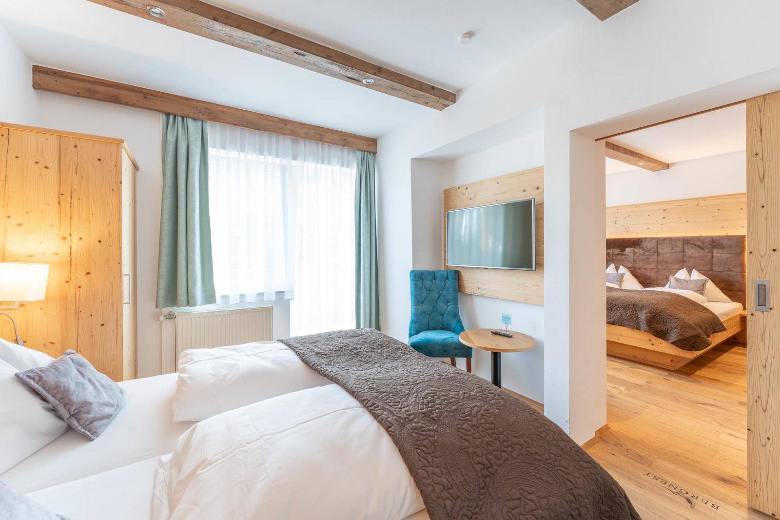 Geräumiges Schlafzimmer mit Holzboden, großem Fenster und Blick in einen weiteren Schlafbereich.