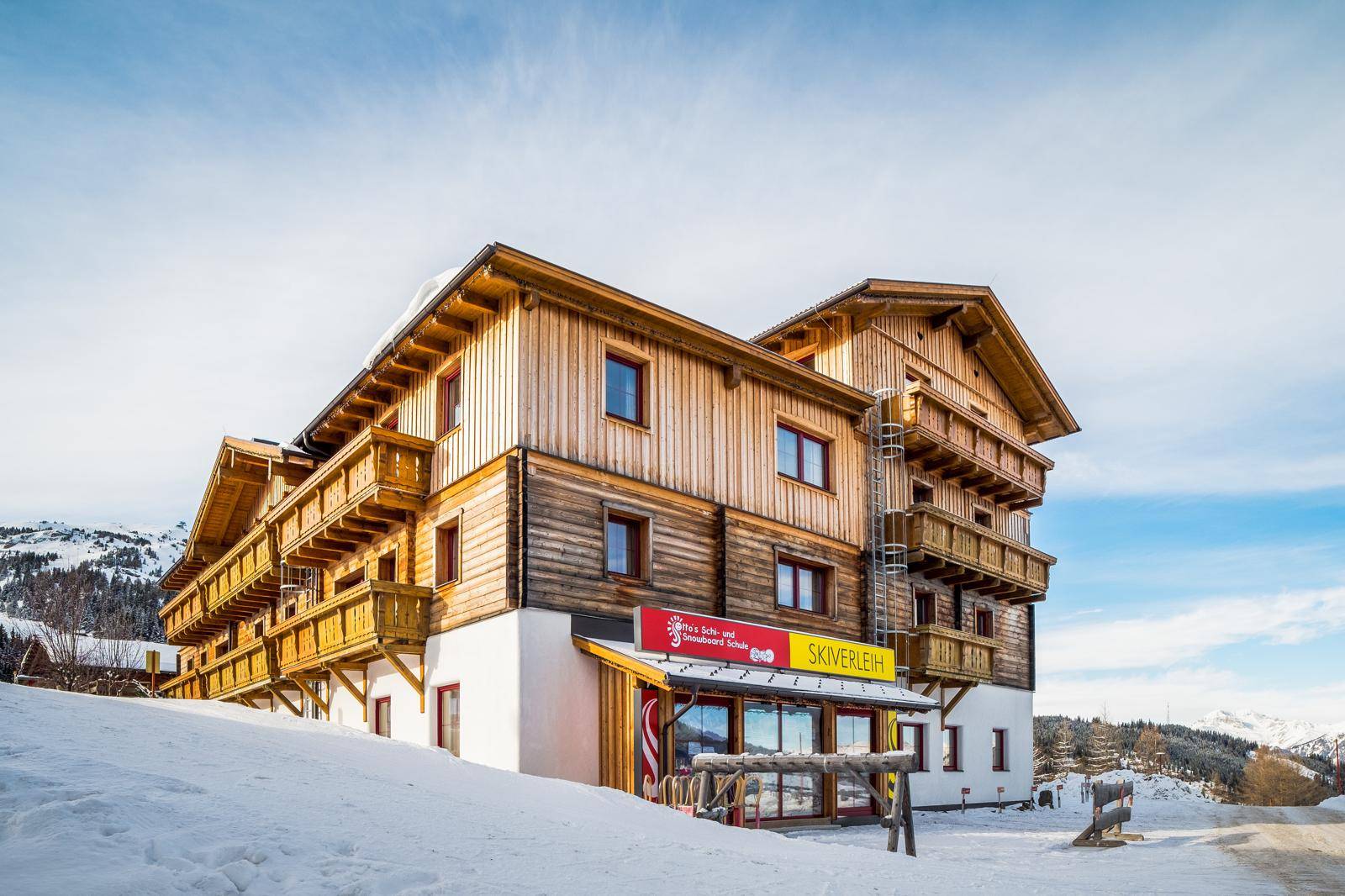 Traditionelles Holzgebäude im Winter mit verschneiter Landschaft und Skiverleih im Erdgeschoss.