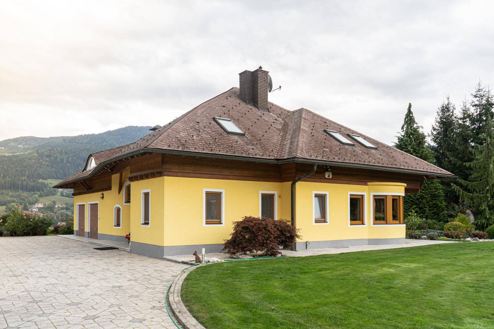 Seitenansicht des gelben Hauses mit braunem Ziegeldach und gepflegtem Vorgartenbereich.