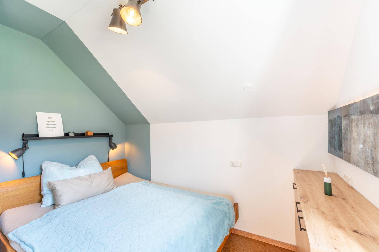 Gemütliches Schlafzimmer mit Holzbett, schräger Wand und moderner Beleuchtung.