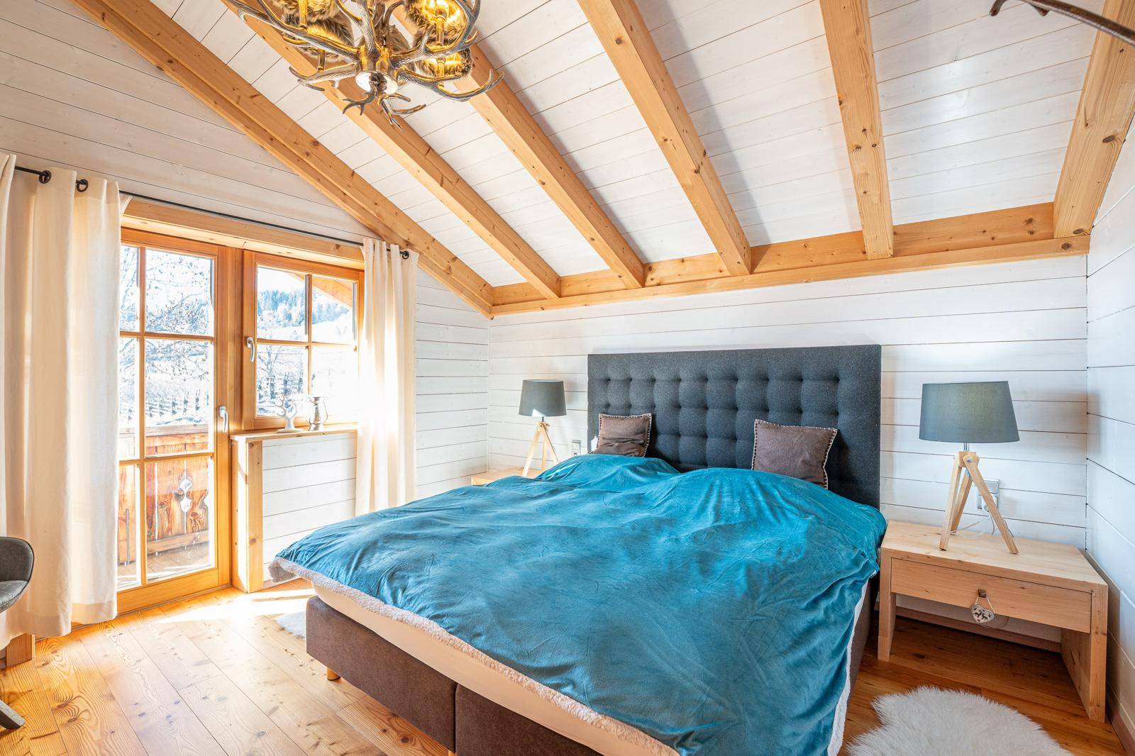 Gemütliches Schlafzimmer mit Holzbalkendecke, Holzboden und Zugang zu einem französischen Balkon.