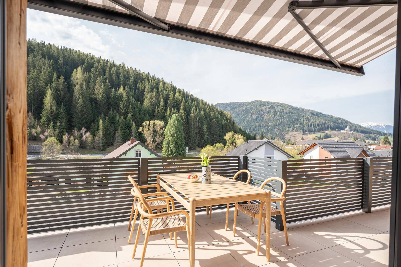 Sonnige Terrasse mit Esstisch, Markise und Panoramablick auf die Berge.