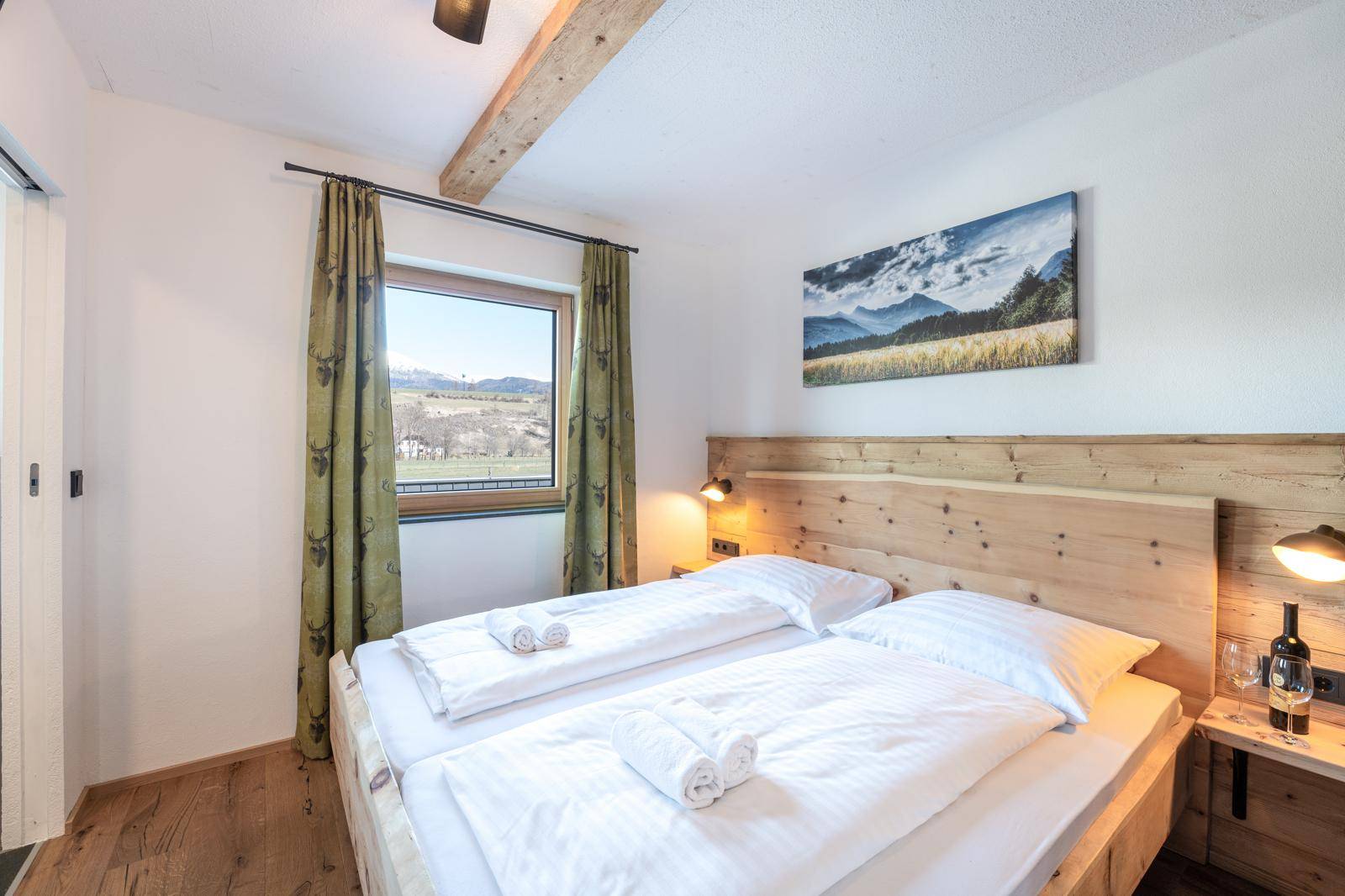 Helles Schlafzimmer mit Holzbett, Holzbalken und Fenster mit weitem Ausblick.