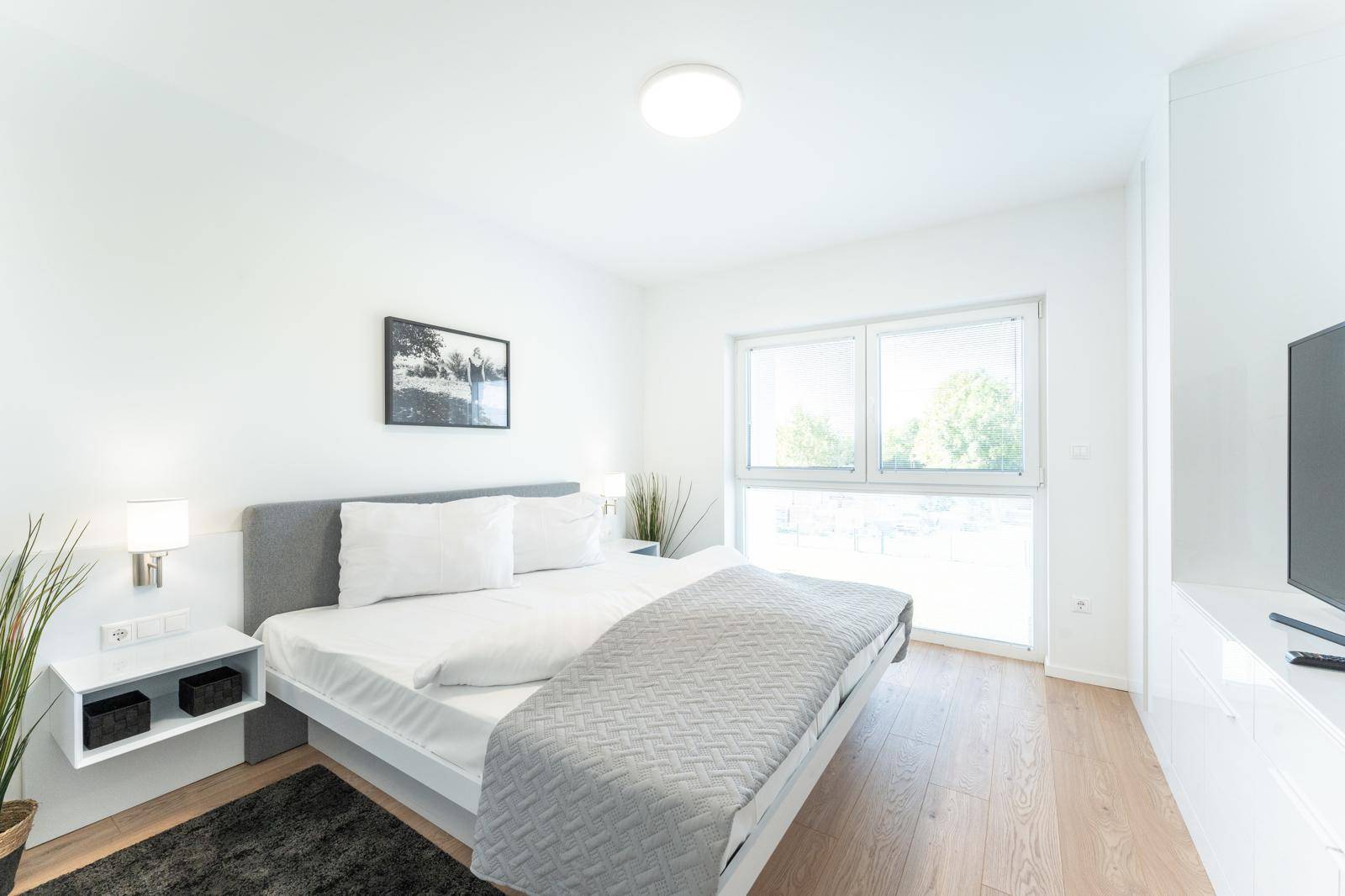 Modernes Schlafzimmer mit Doppelbett, Holzboden und großem Fenster für viel Tageslicht.