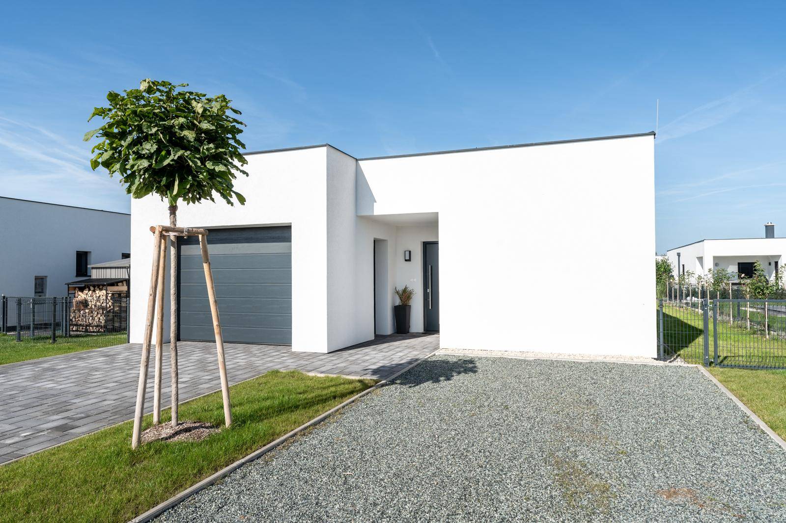 Vorderansicht eines modernen Einfamilienhauses mit integrierter Garage und Kiesauffahrt unter blauem Himmel.