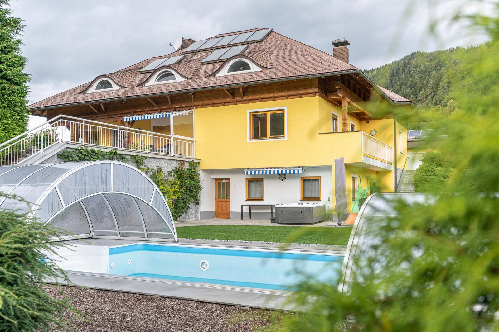 Rückansicht des Hauses mit überdachtem Pool, Whirlpool und Zugang zu einer Terrasse.