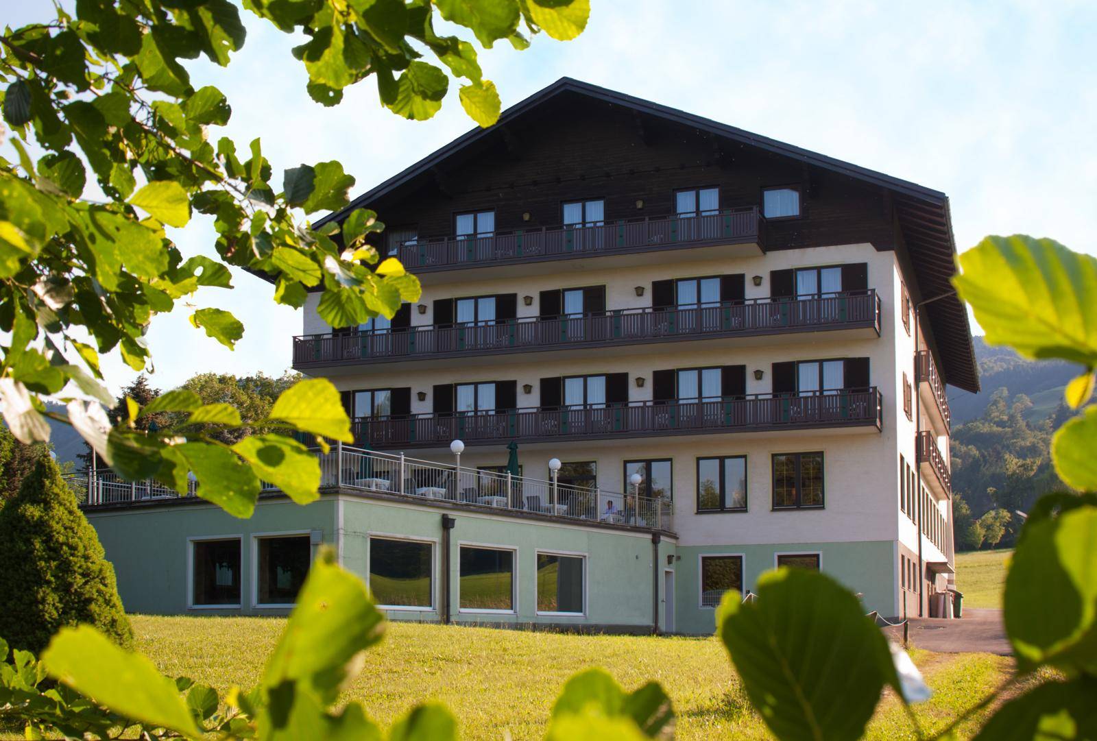 Gebäudeansicht von einer grünen Wiese aus, mit Balkonen und einer Terrasse im Vordergrund.