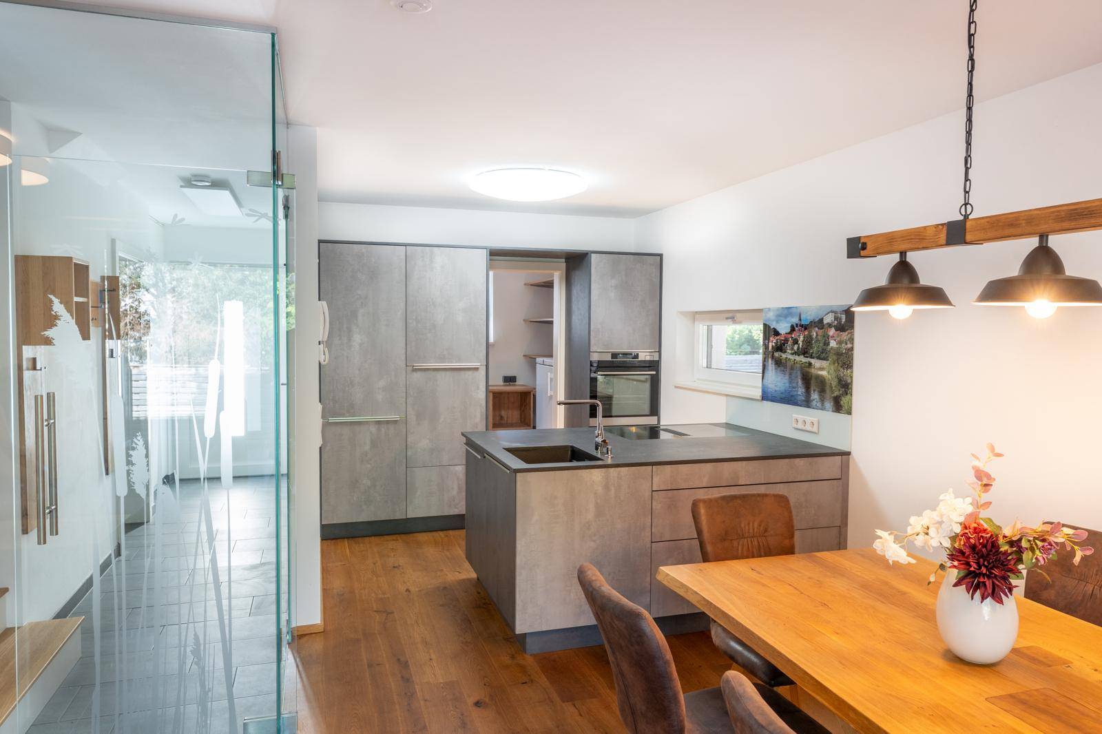 Moderne Einbauküche mit grauen Fronten, integrierten Geräten und Essbereich.