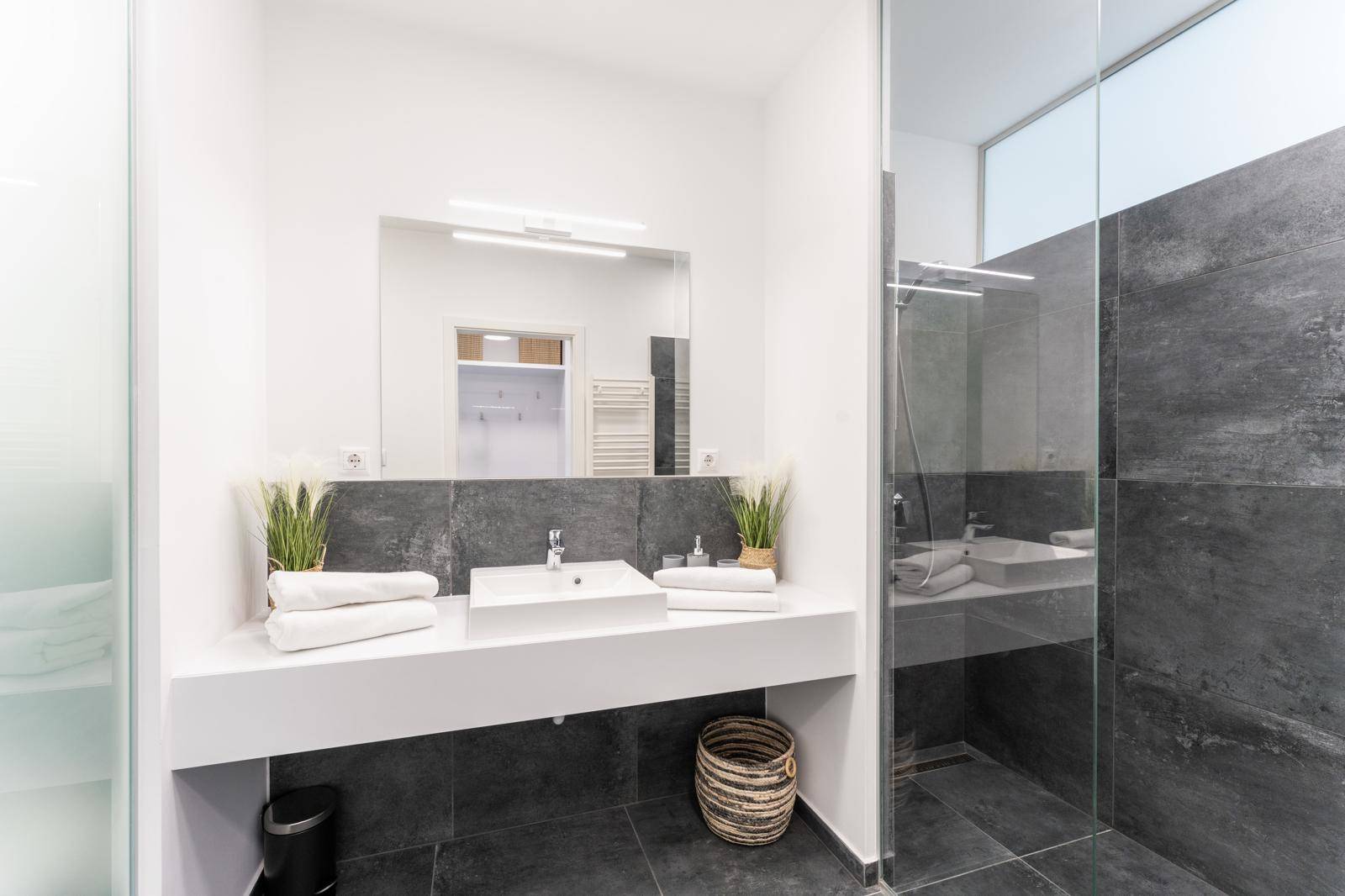 Modernes Badezimmer mit großer begehbarer Dusche, Einzelwaschbecken und dunklen Fliesen.
