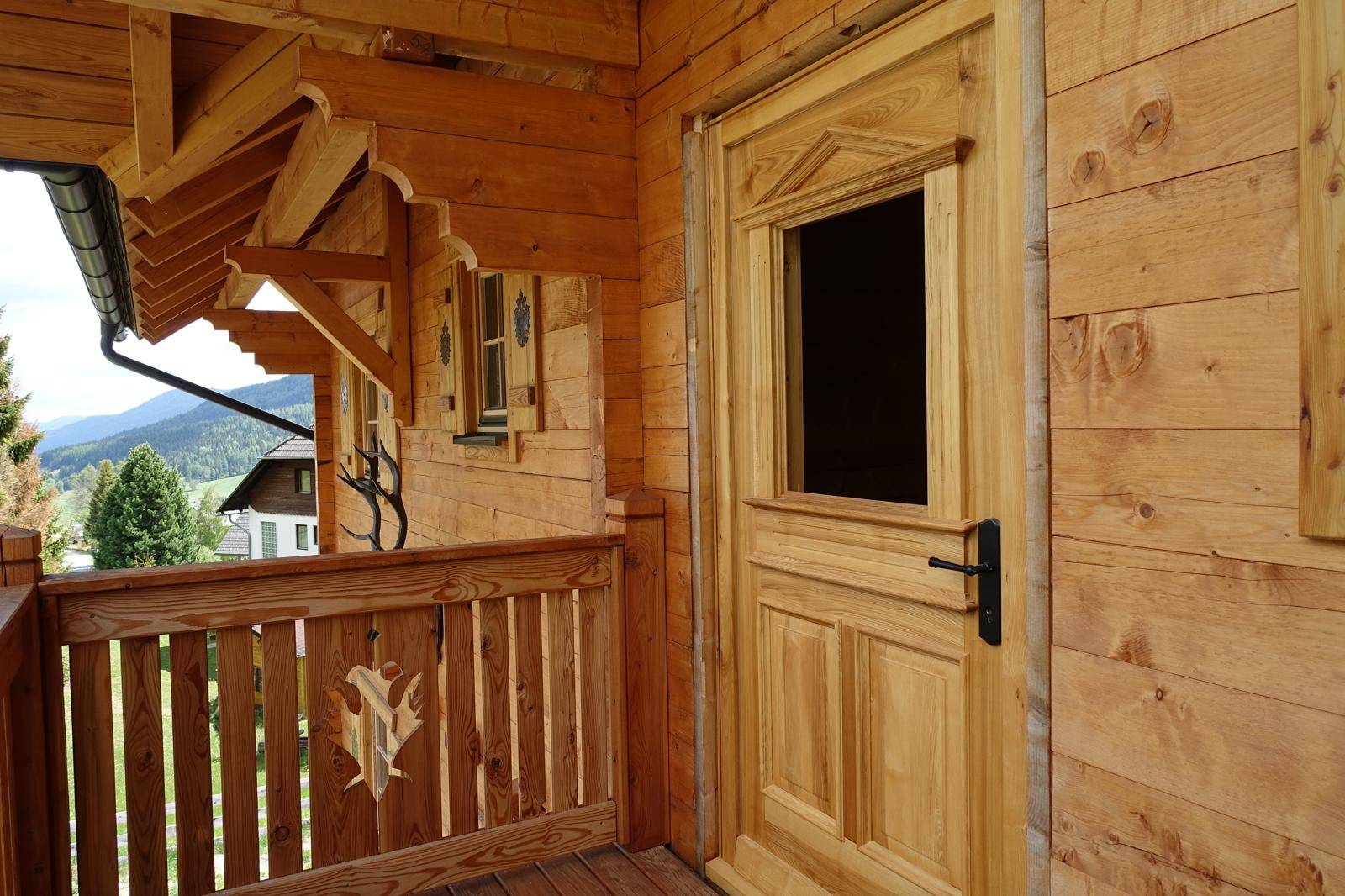 Detailansicht eines Holzbalkons mit geschnitztem Geländer und traditioneller Holztür.